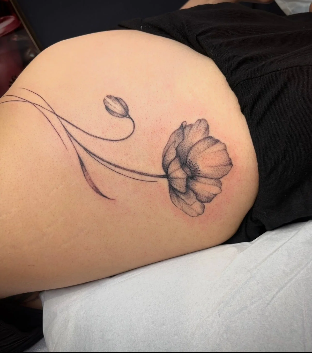 A black and gray floral tattoo of a blooming flower with a smaller bud on a person's upper arm.