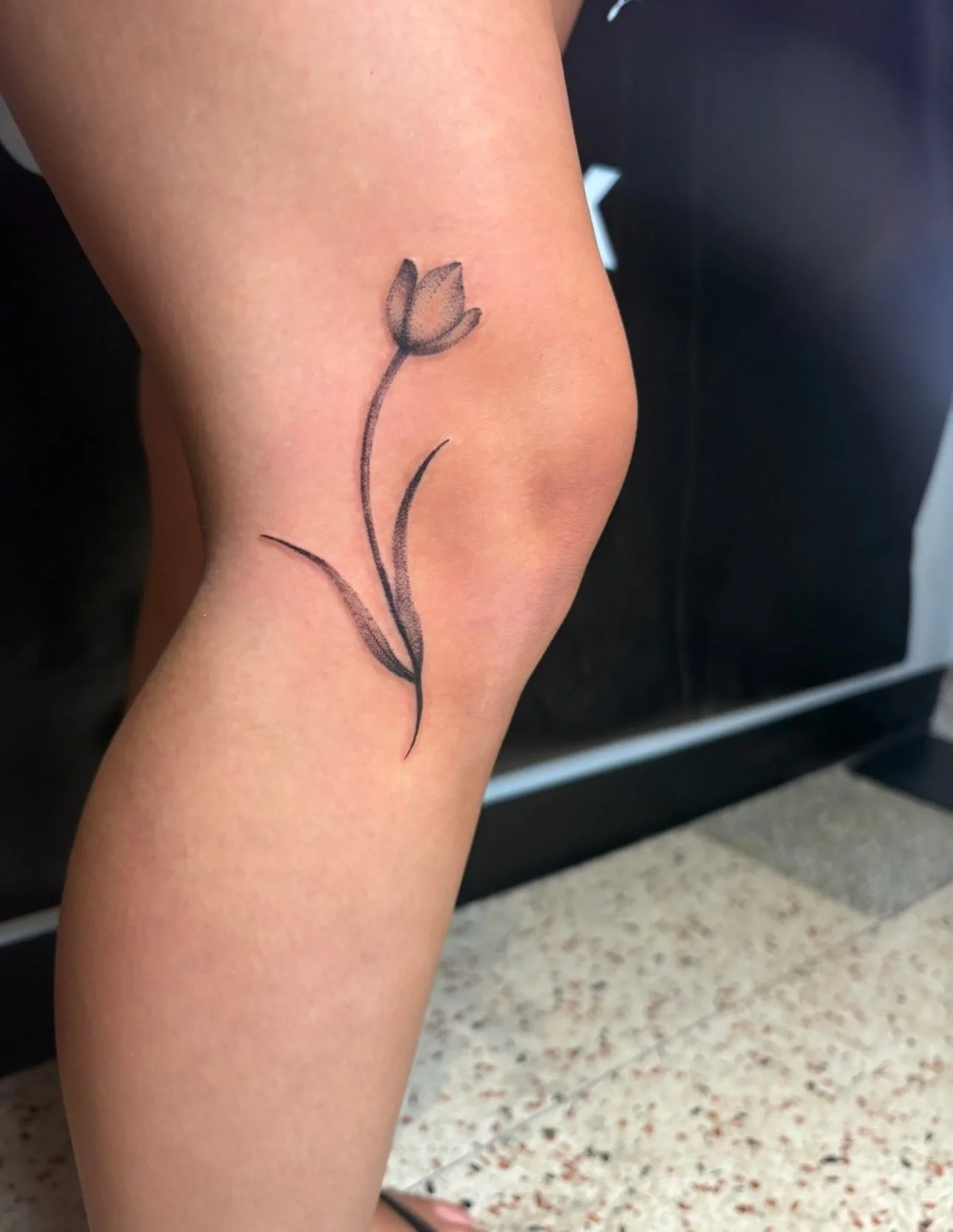 Tattoo of a simple flower with a curved stem and two leaves on person's upper thigh.