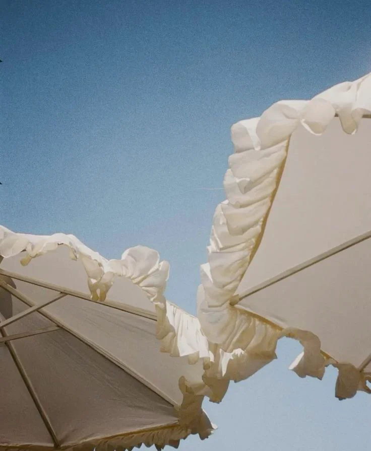 Close-up of torn, scalloped white beach umbrellas against a blue sky.