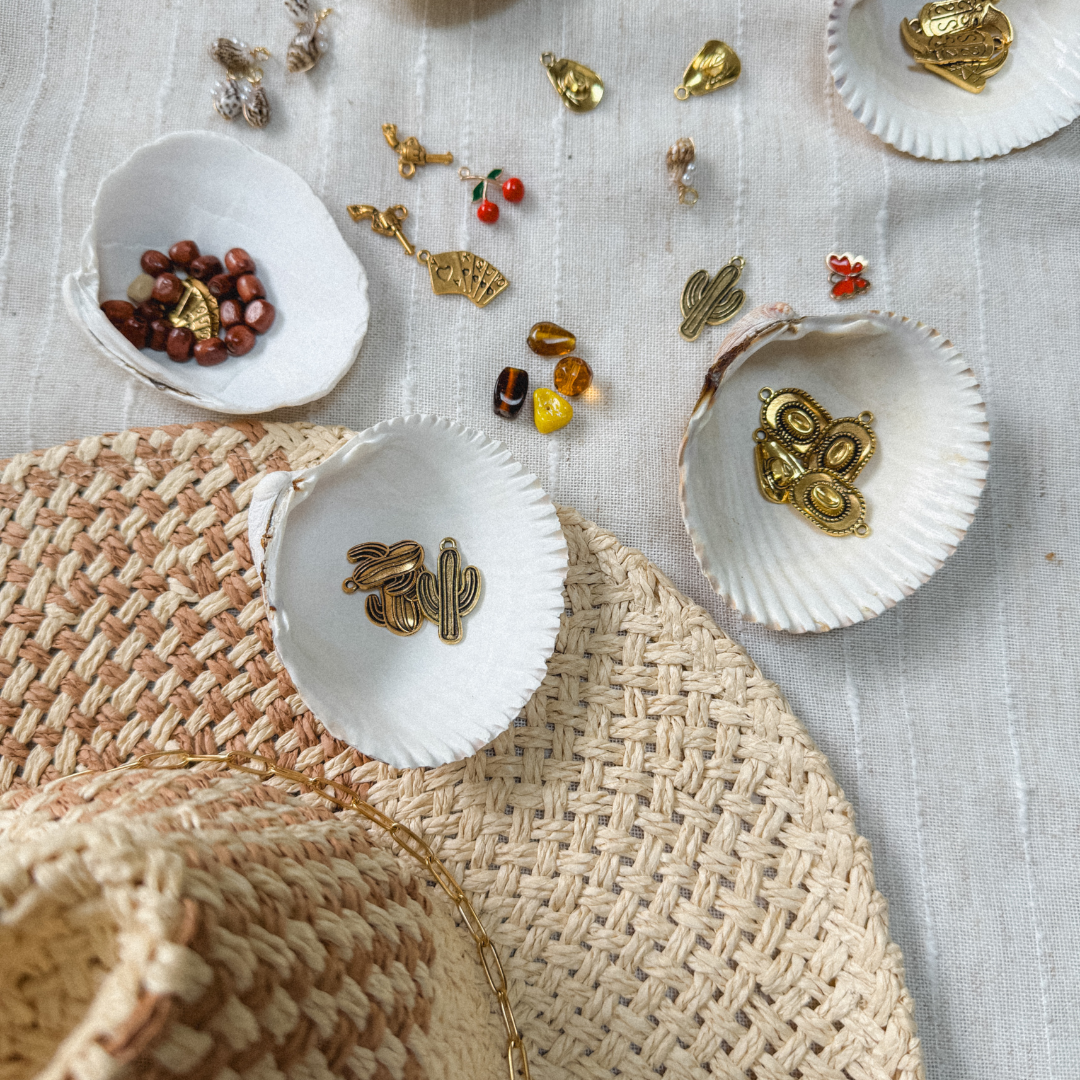 Assorted jewelry and decorative items on a white cloth background, including gold charms, small beads, and seashells.