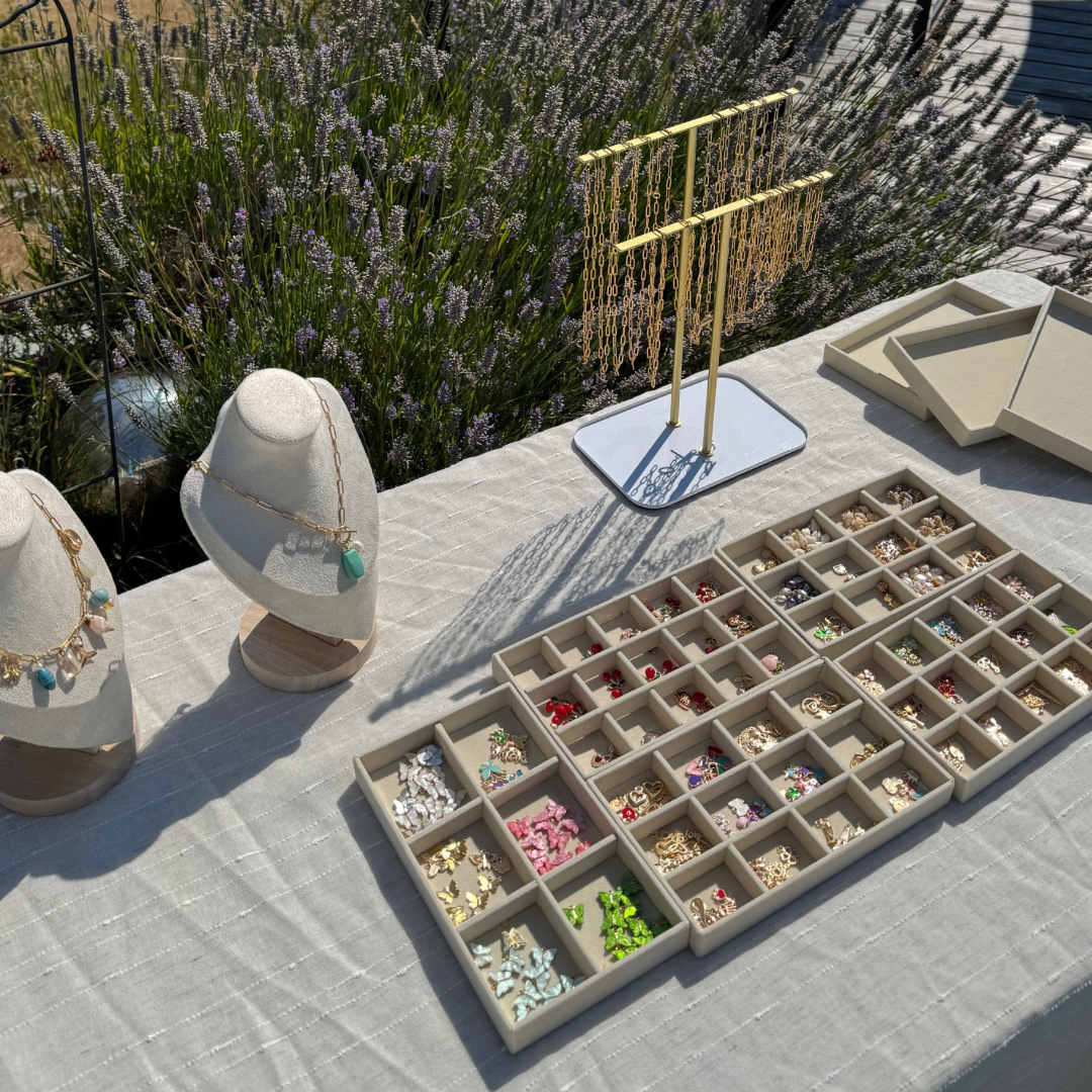 Jewelry display table with necklaces on busts, earrings in a tray, and chains on a jewelry stand, outdoors with lavender plants in the background. Located in the Cowichan Valley.