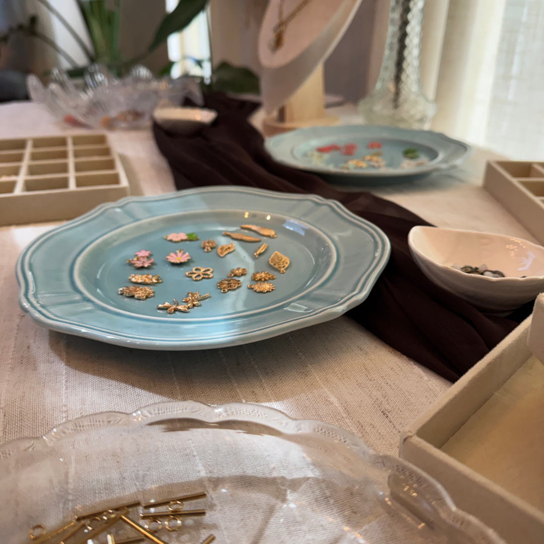 Various small jewelry charms and findings, including flowers and animals, placed on ceramic and glass dishes on a table surface.