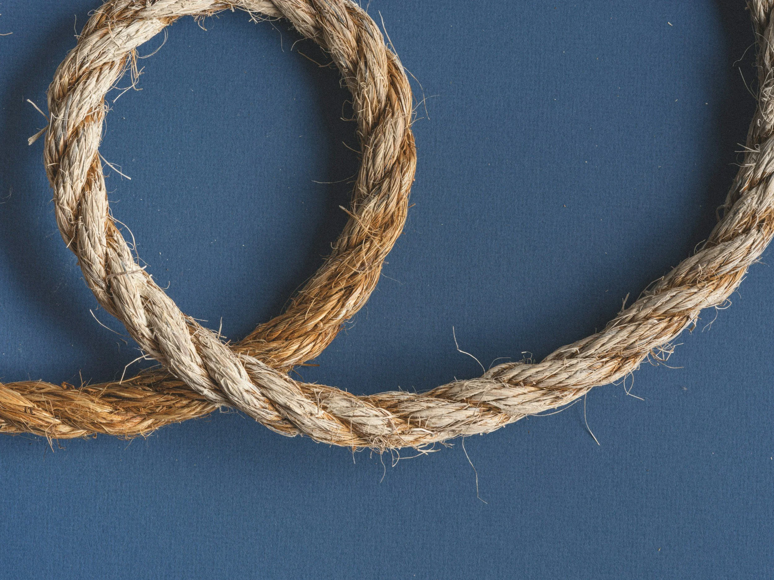 Close-up of frayed, intertwined beige and brown rope on a dark blue background.