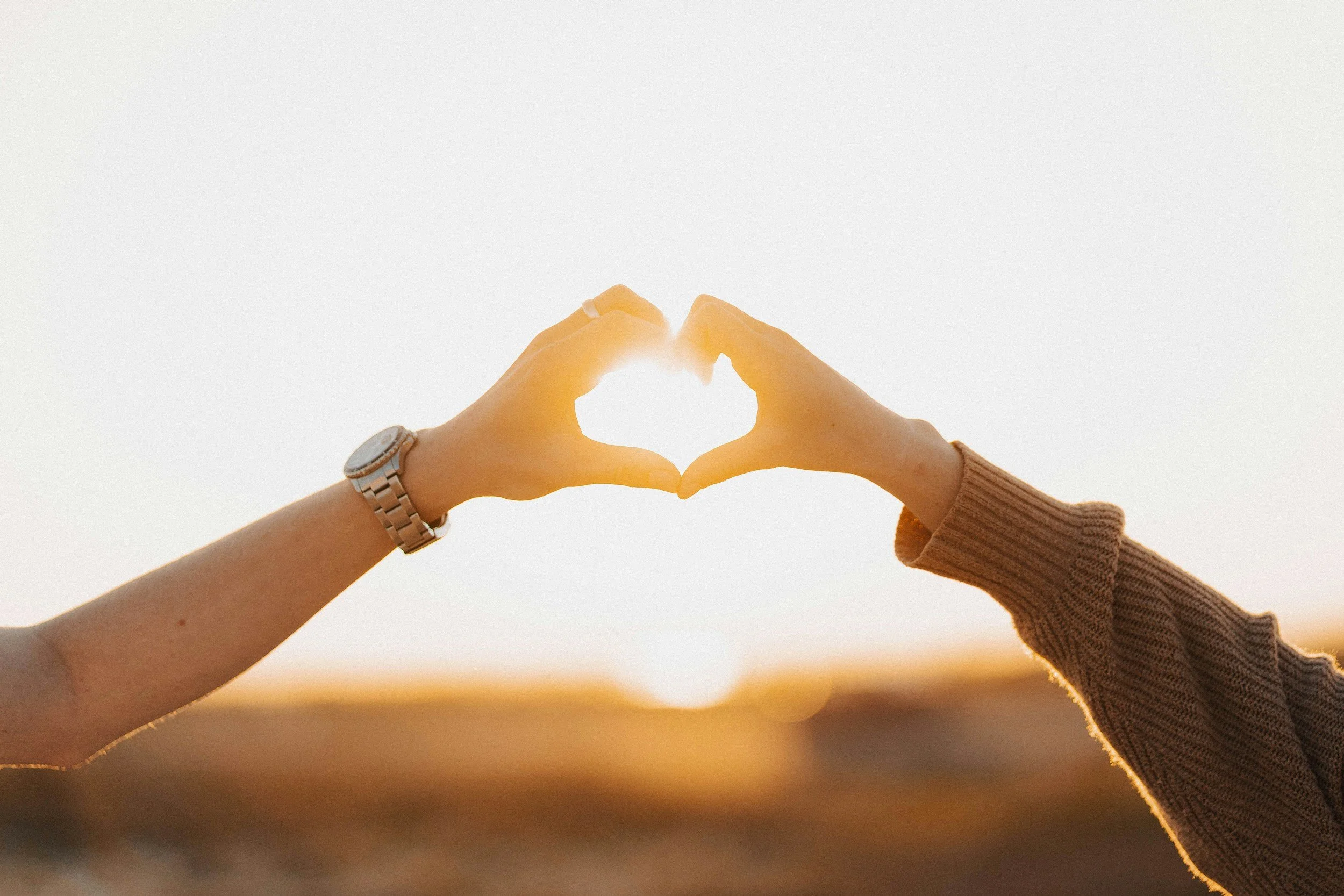 Two hands forming a heart shape with the sunset in the background.