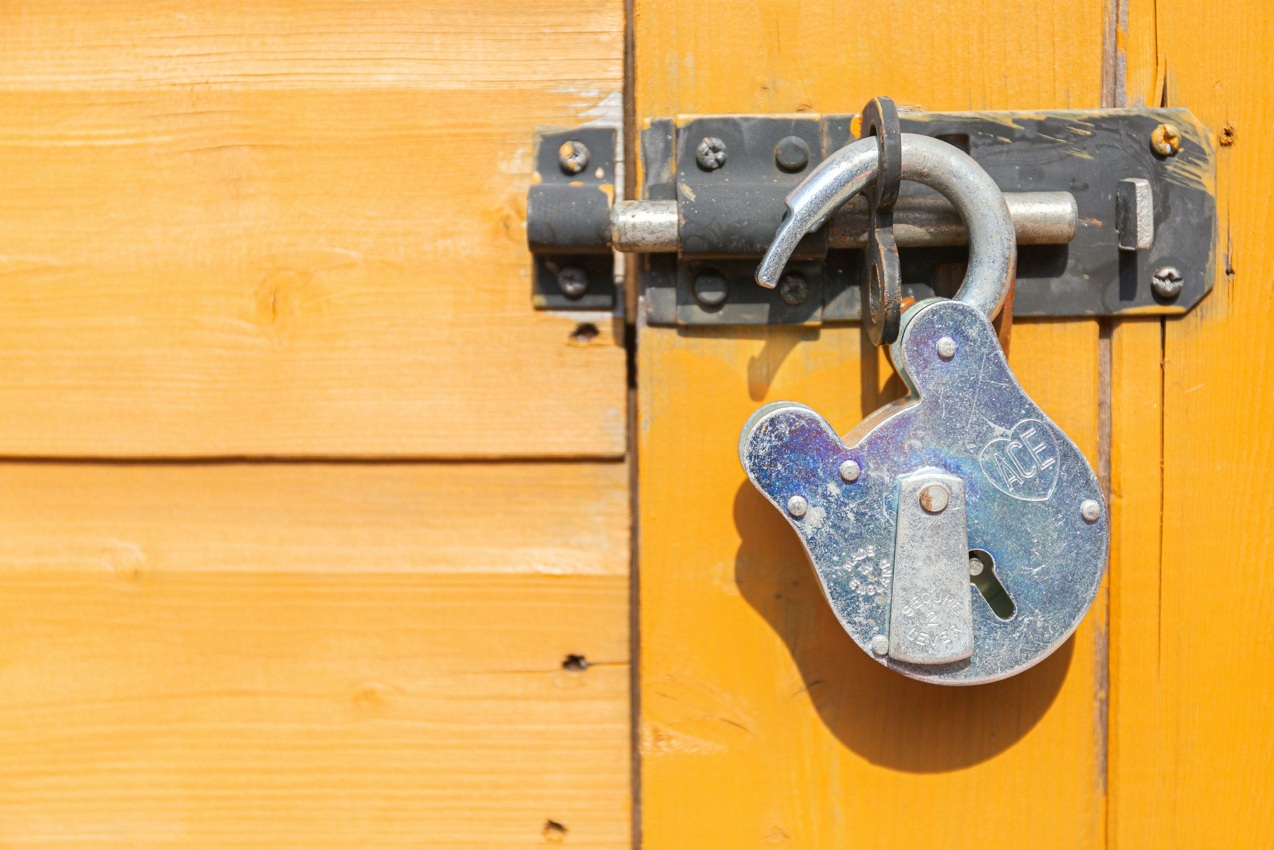 A wooden door with a metal latch and a large padlock for security.