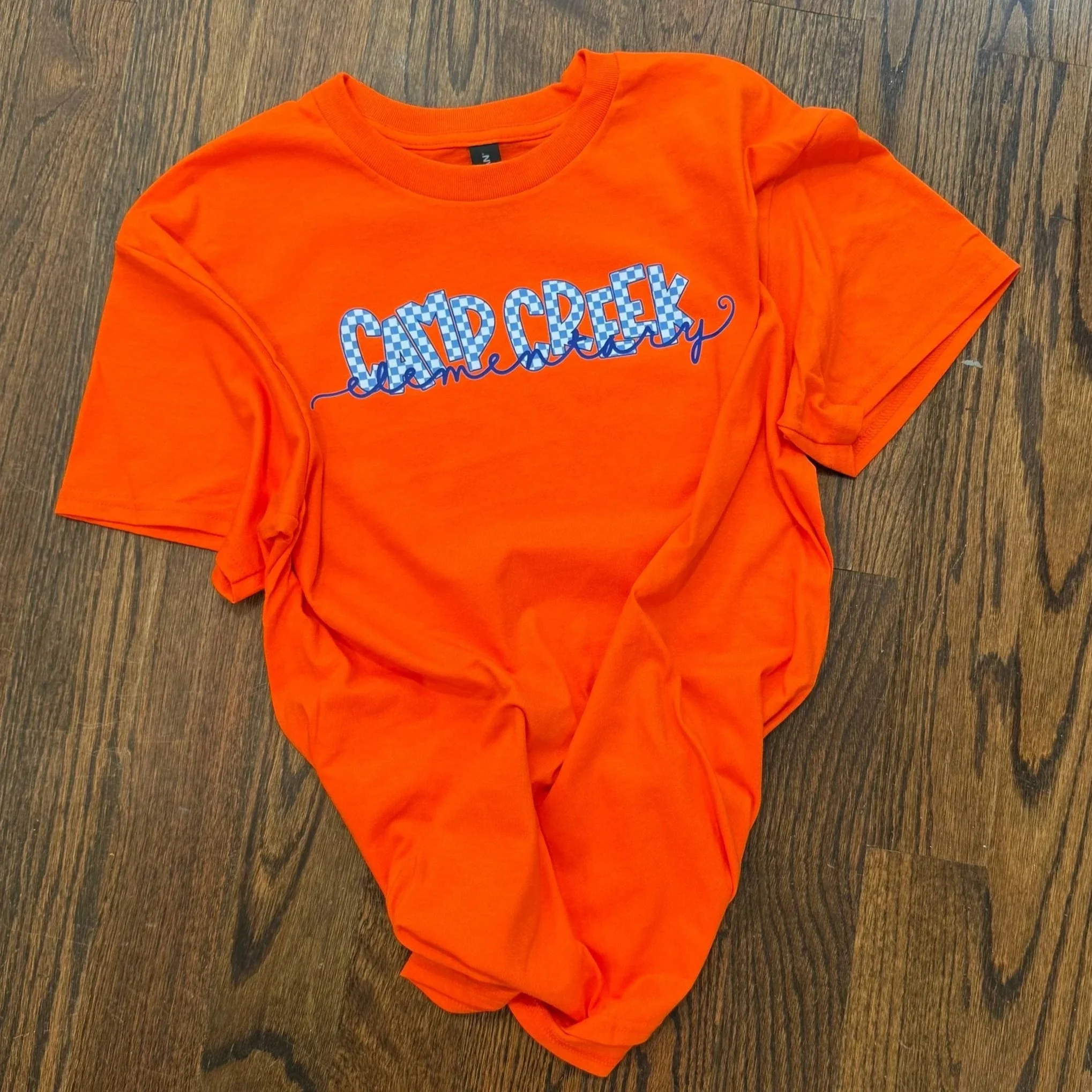 Bright orange T-shirt with a graphic design, laid on a wooden surface.