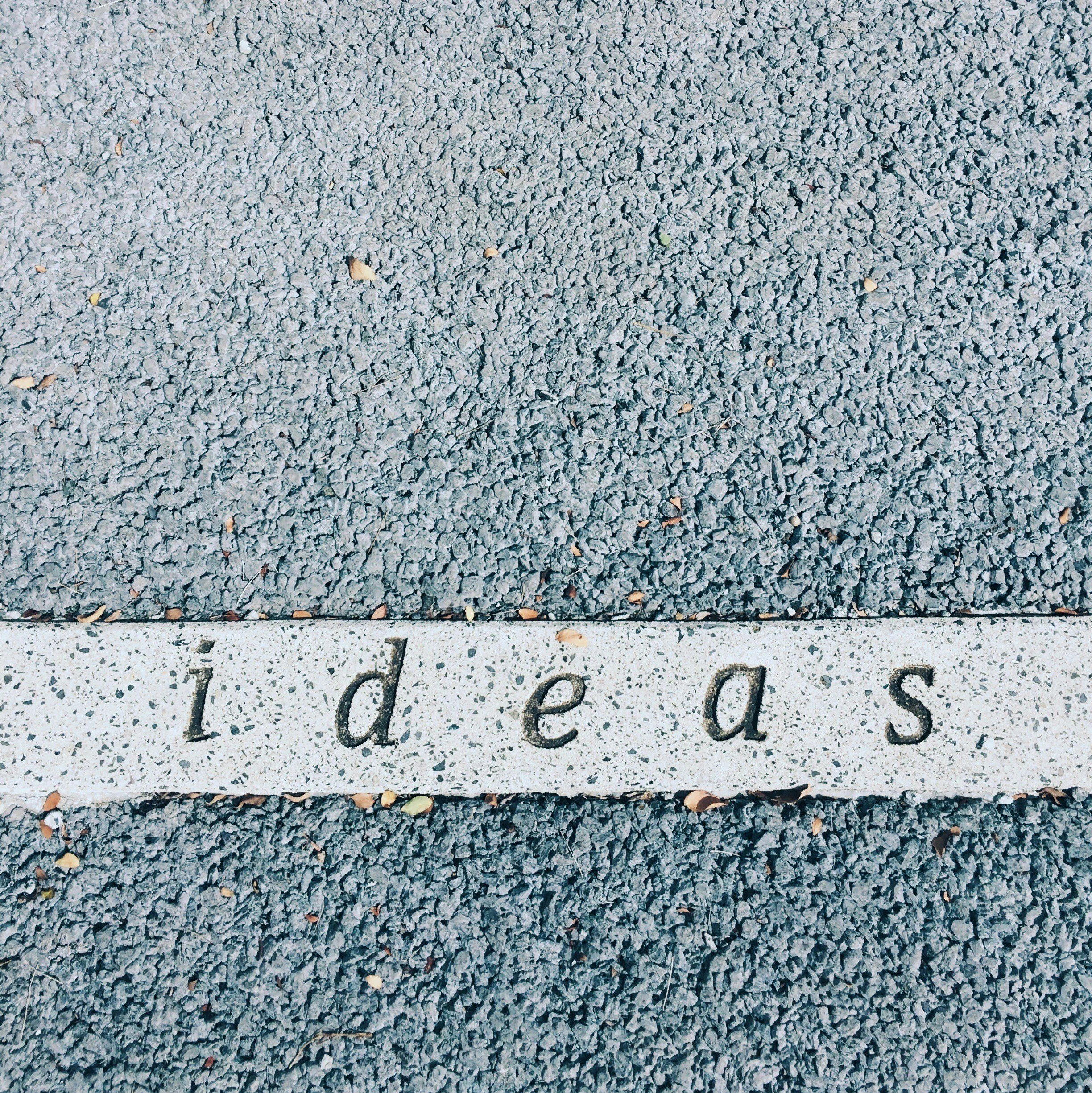 Close-up of a textured concrete surface with scattered fallen leaves and the word "ideas" carved into the surface.