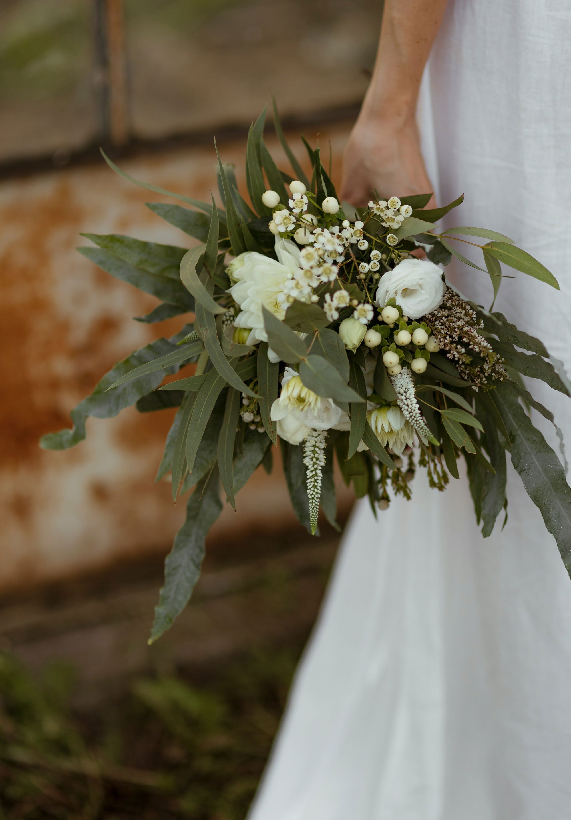 Bride holding a bouquet of white flowers and greenery, with part of a white dress visible.