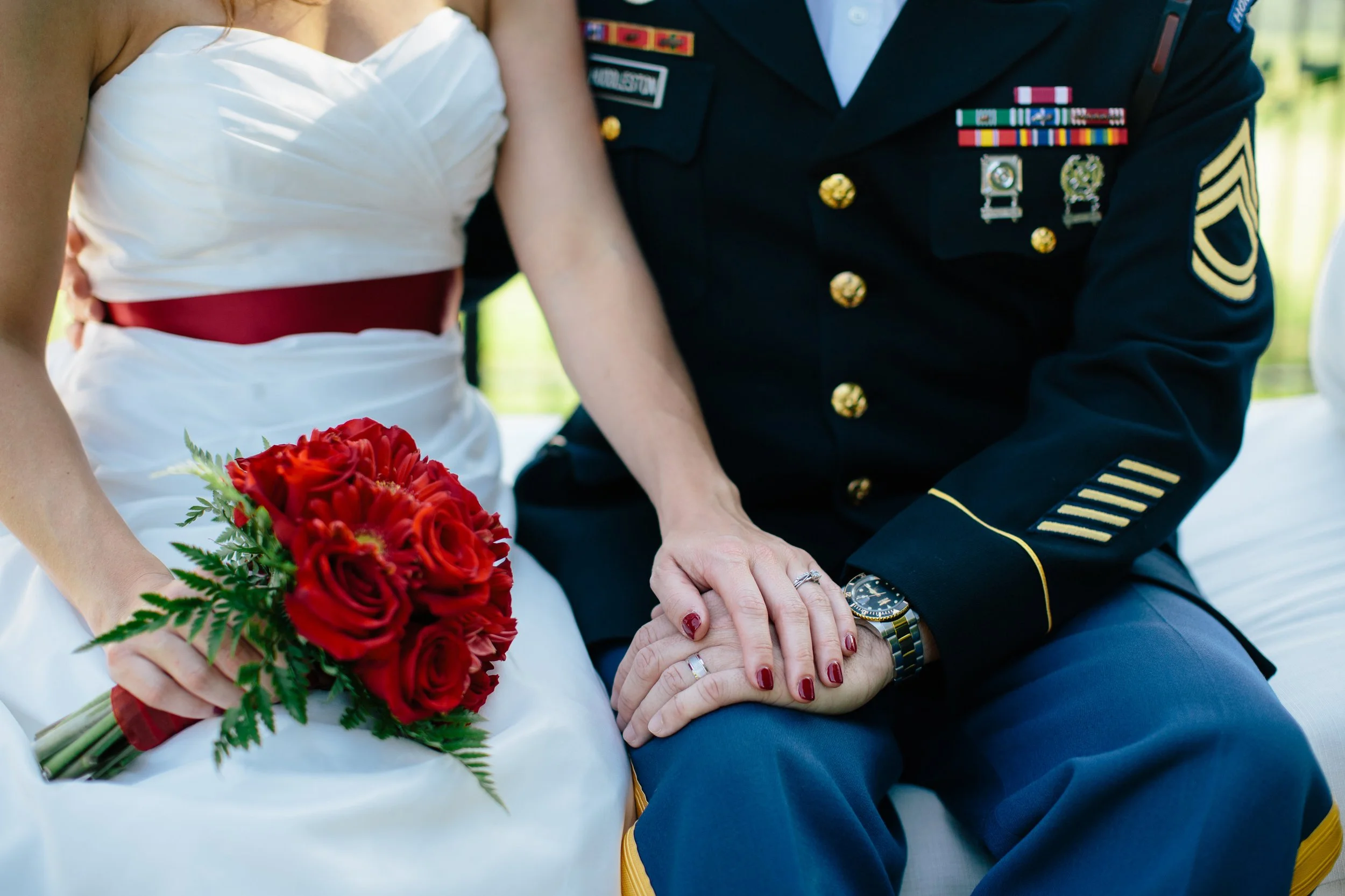 A bride and a groom holding hands, with the bride holding a bouquet of red roses and the groom in a military uniform with medals.