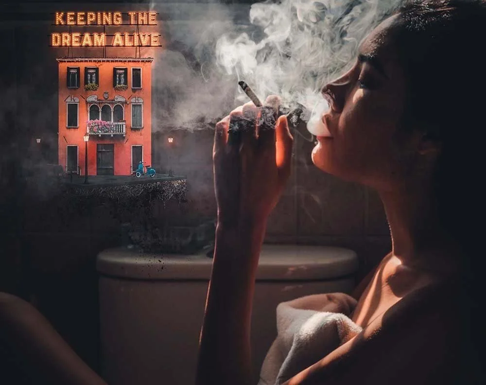 A woman smoking a cigarette in a dimly lit room with a surreal projection of a colorful building with a neon sign that reads 'Keeping the Dream Alive,' and a blue bicycle parked outside.
