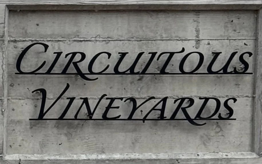 Sign reading 'Circoutous Vineyards' mounted on a wooden wall.