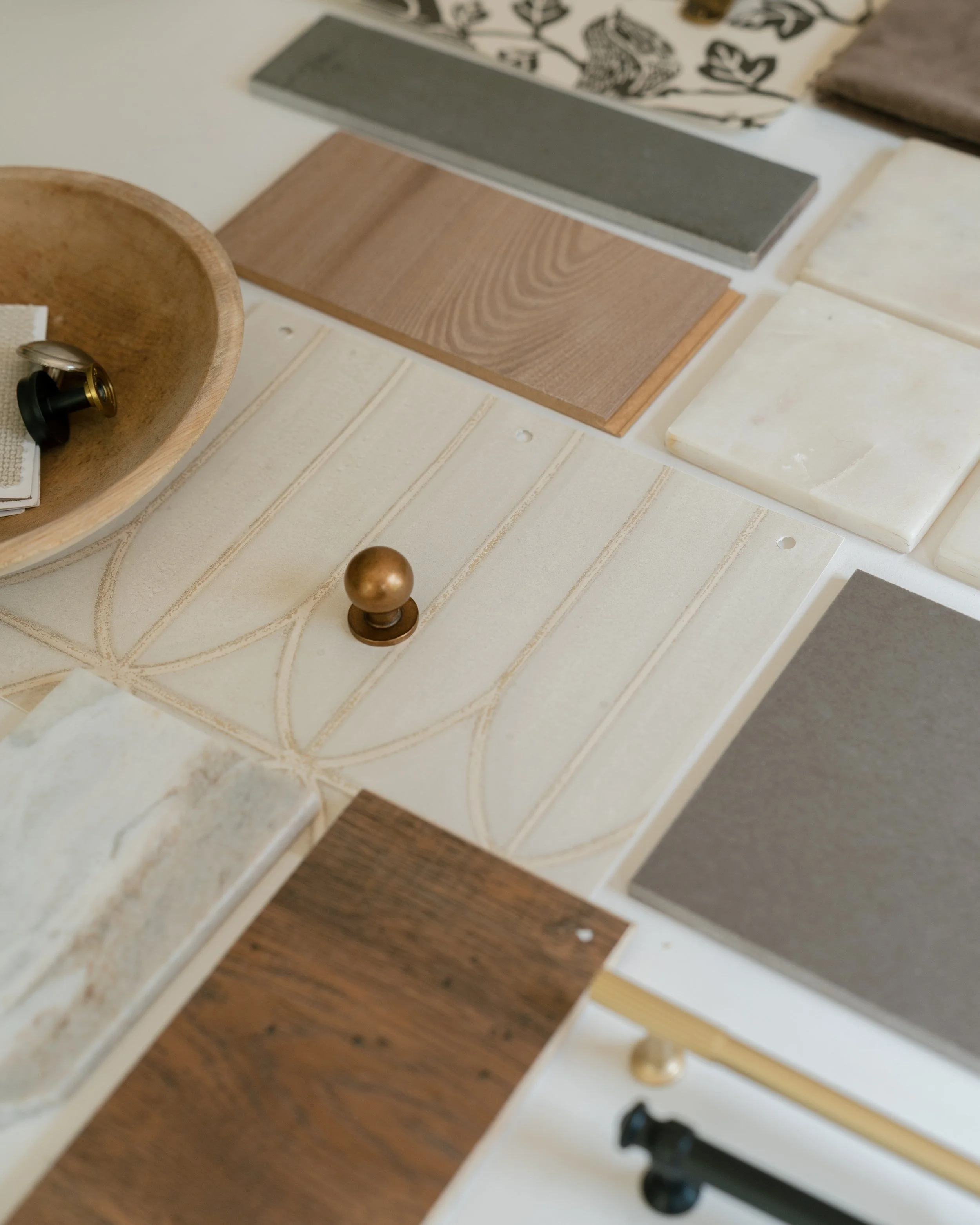Flat lay of design materials for an interior design new build project. Display of various tile samples arranged on a table, including wood-look, stone-look, and patterned tiles. Wallpaper and cabinet hardware as well.