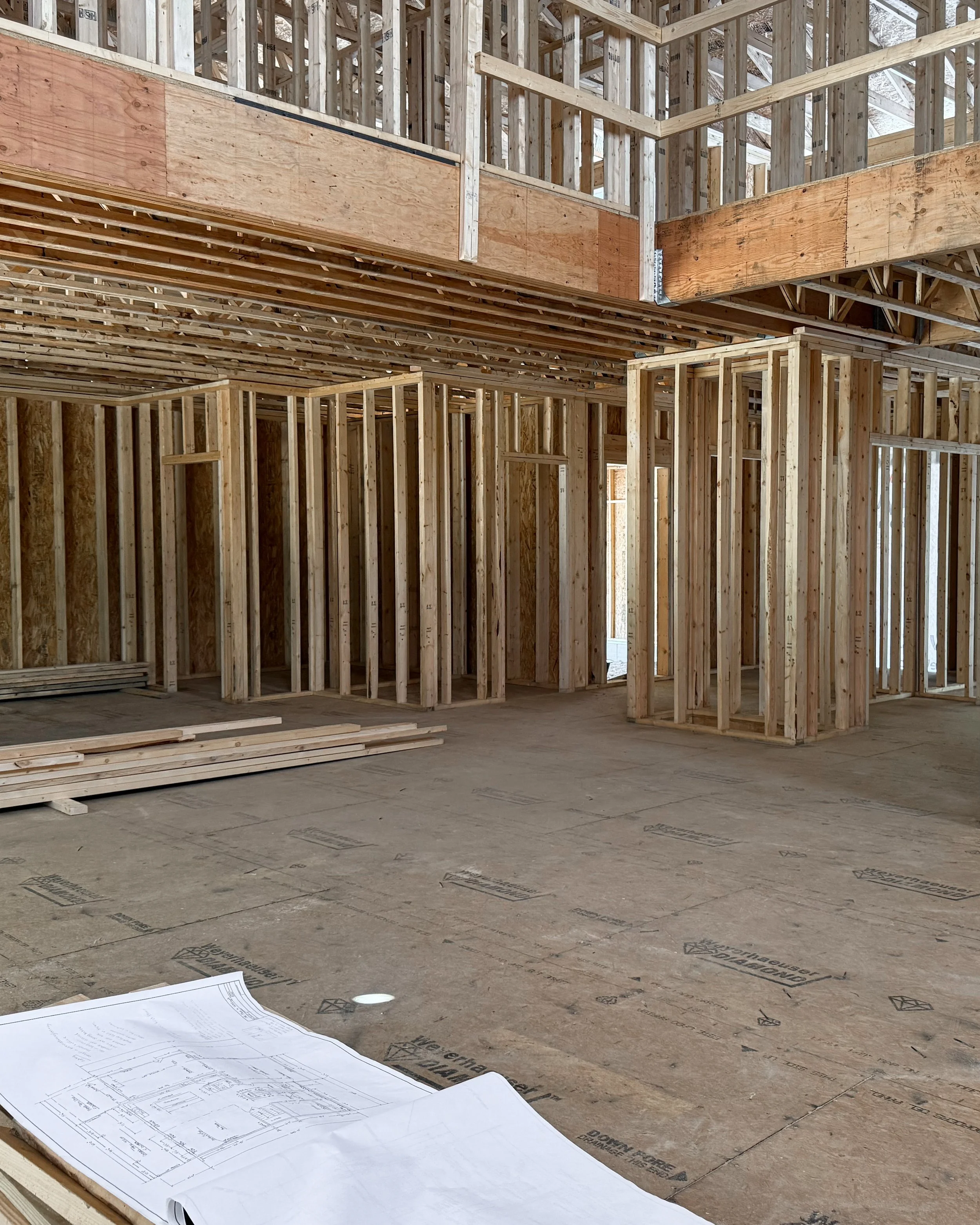 Interior view of a building under construction with wooden framing and some architectural blueprints on the floor.