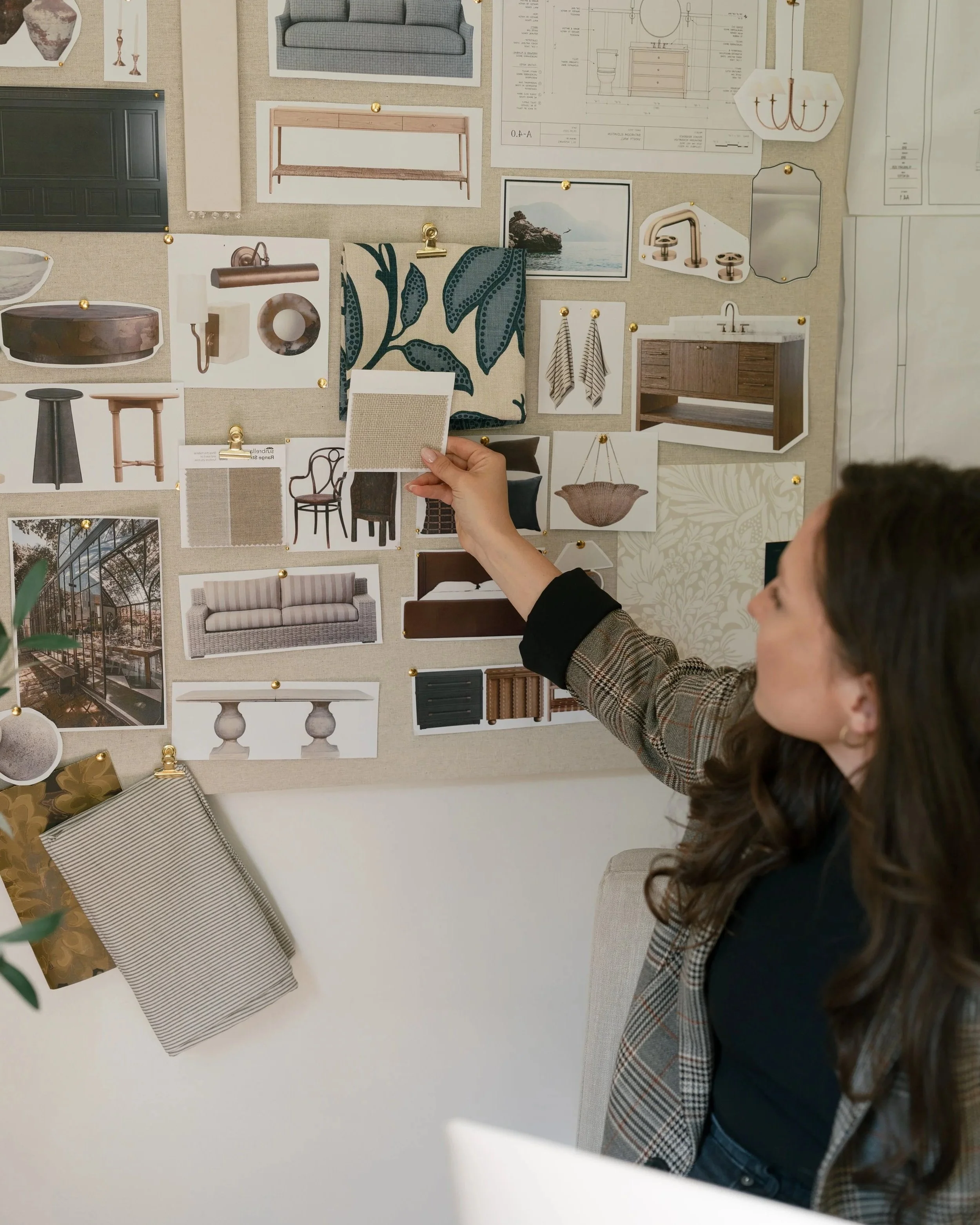 Interior design mood board with fabric samples, furniture images, and architectural plans pinned on a wall, with a interior designer holding a fabric swatch for a job in Columbus Ohio.