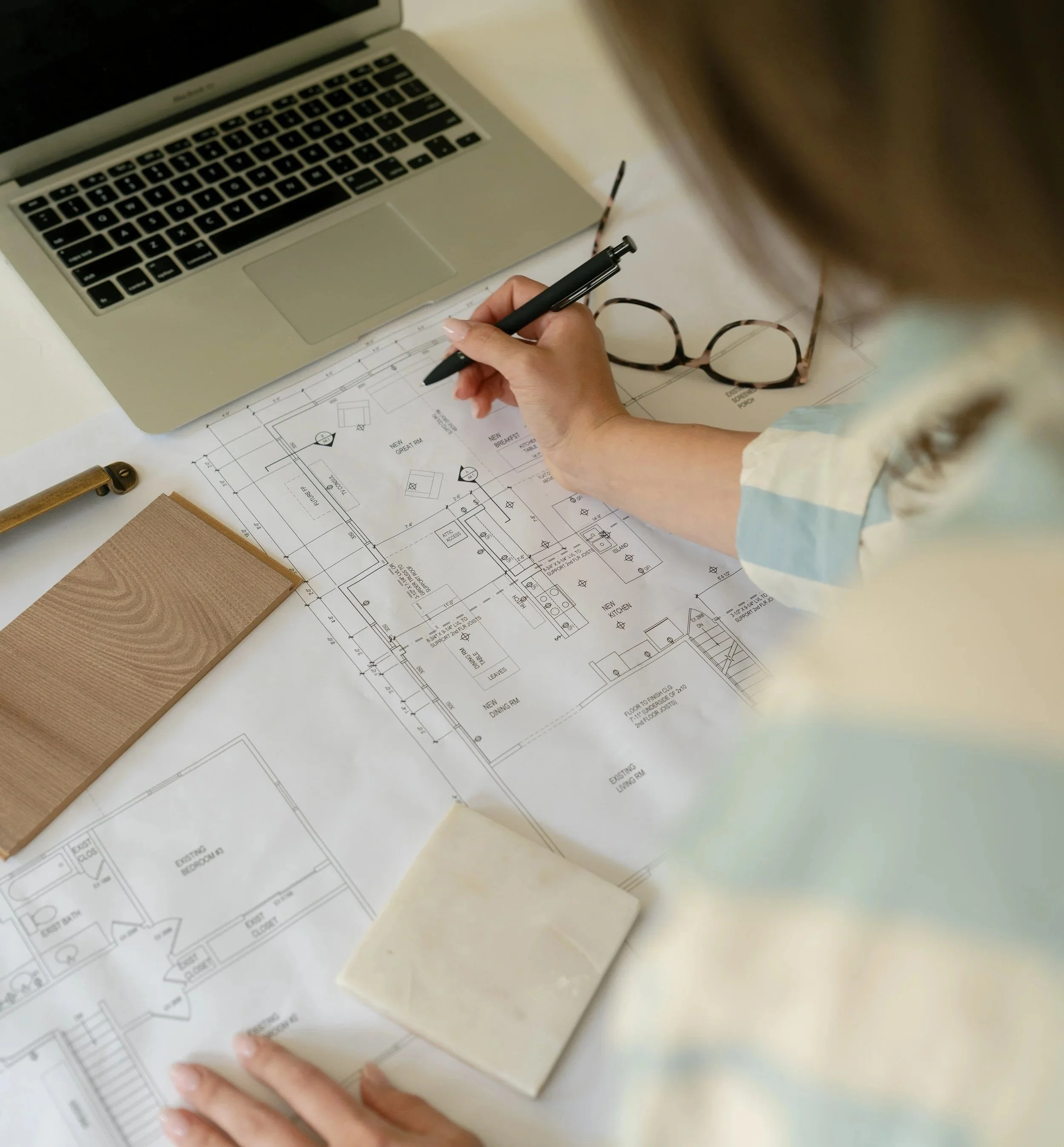 Columbus Ohio Interior Designer working on architectural blueprints with a laptop, glasses, and a notebook on a white table.