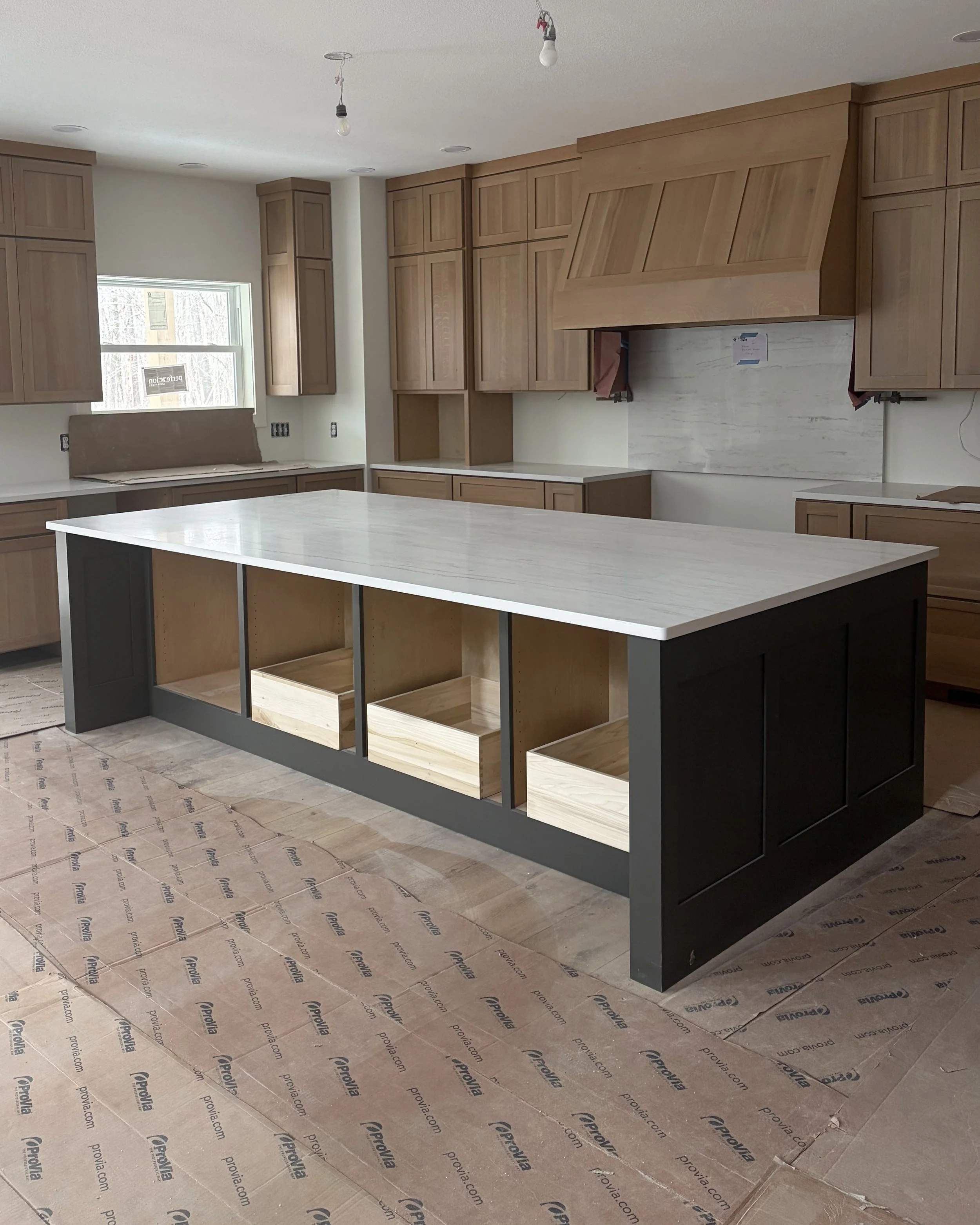 Kitchen under construction with wooden cabinets, a large central island, and protective paper on the floor. This project was a new build in Lexington Ohio.