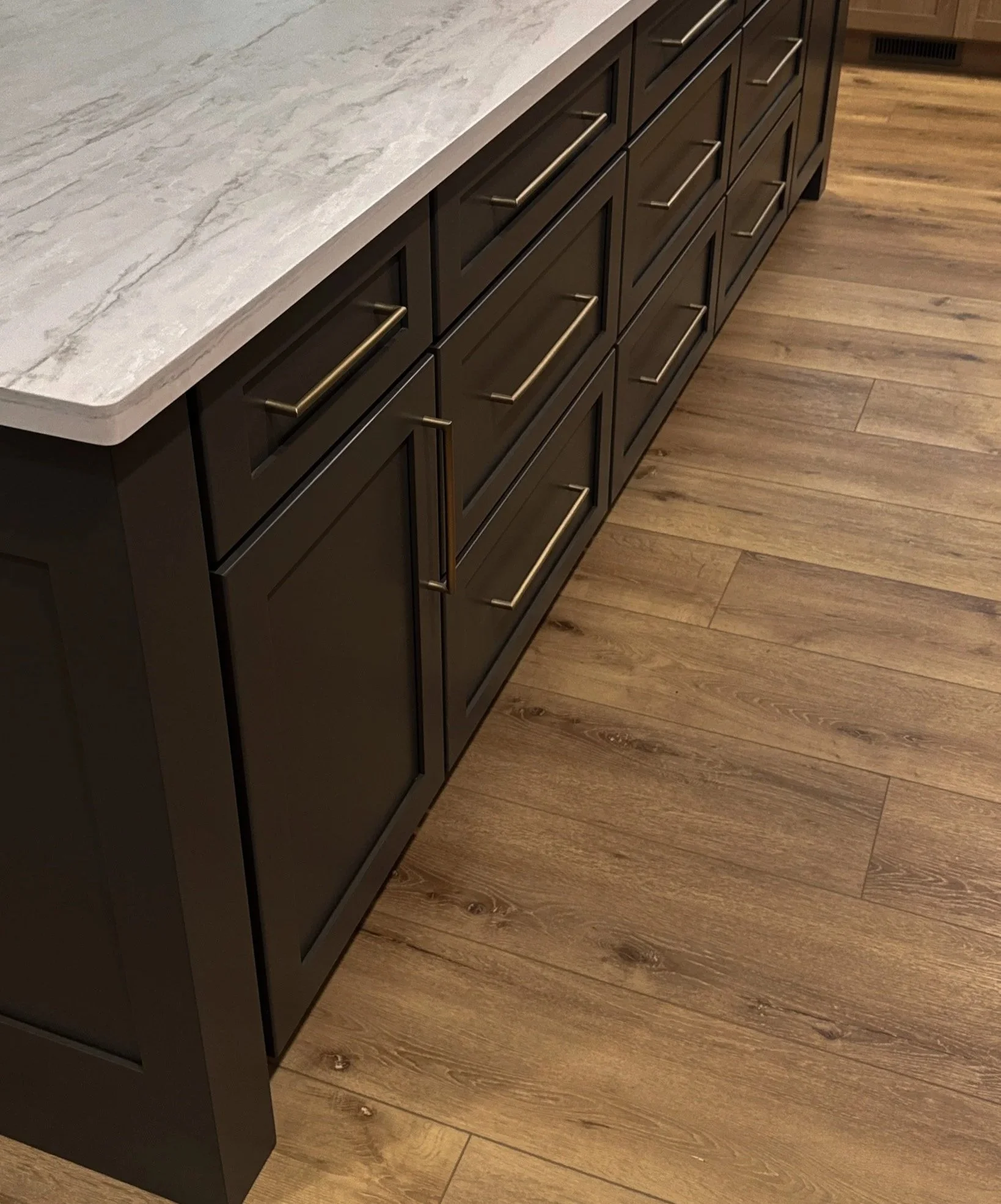 Kitchen cabinet painted in Sherwin William Urbane Bronze (SW 7048). A warm dark black finish and gold hardware, white quartz countertop, and wooden floors.