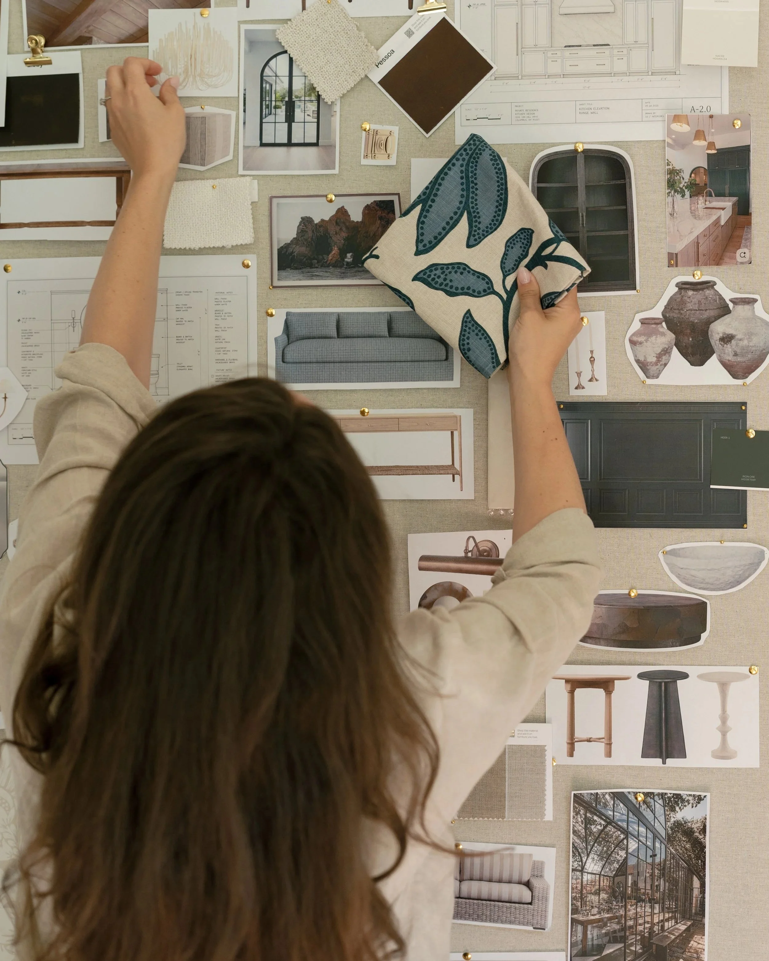 A person is pinning images, fabric samples, and design plans on a fabric-covered board, with a range of interior design inspiration including furniture, architecture, and decor.