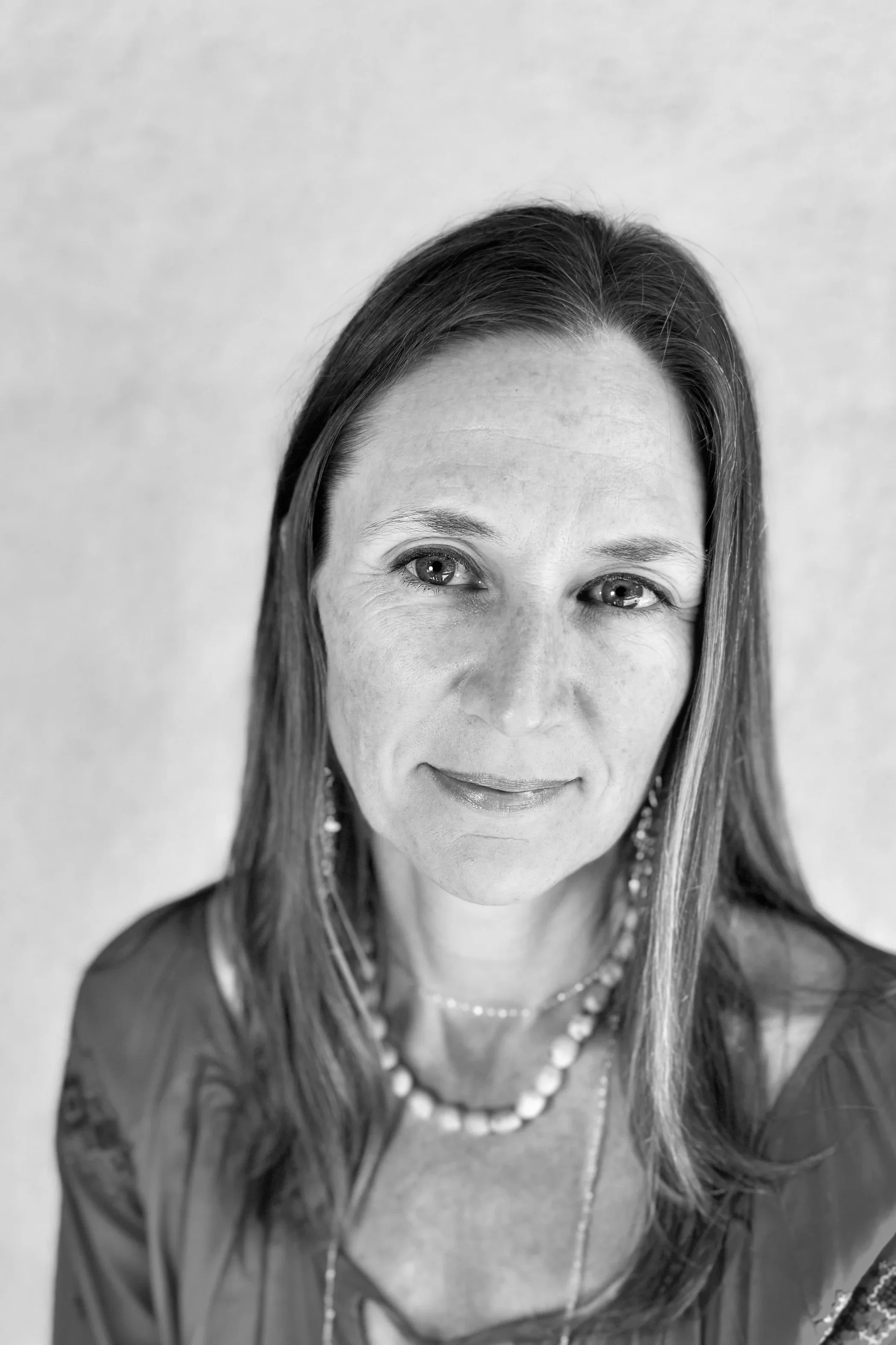 Black and white portrait of author, AJ Olsen, wearing a necklace and earrings, smiling gently, with a neutral background.