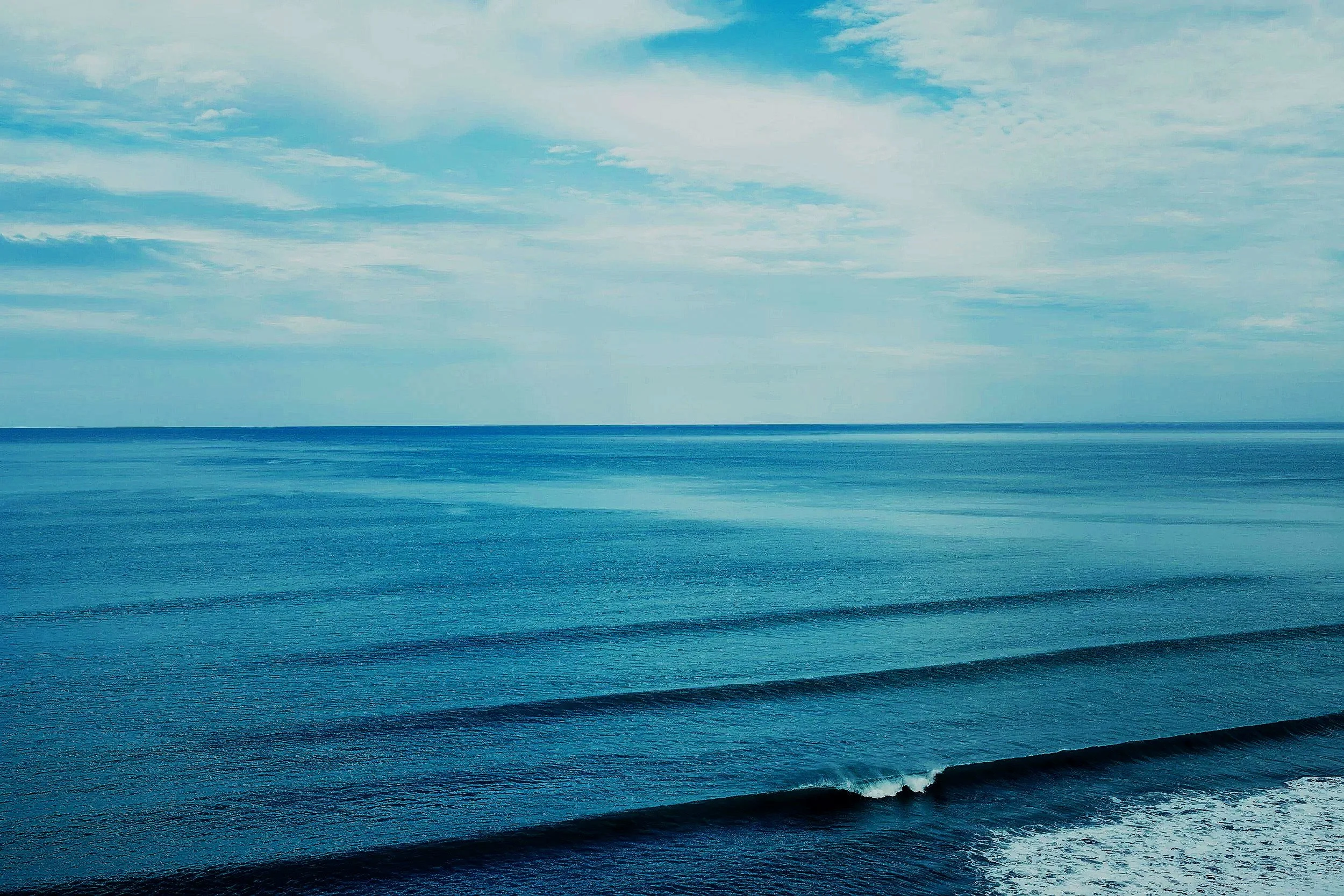 Calm ocean with gentle waves under a partly cloudy sky.
