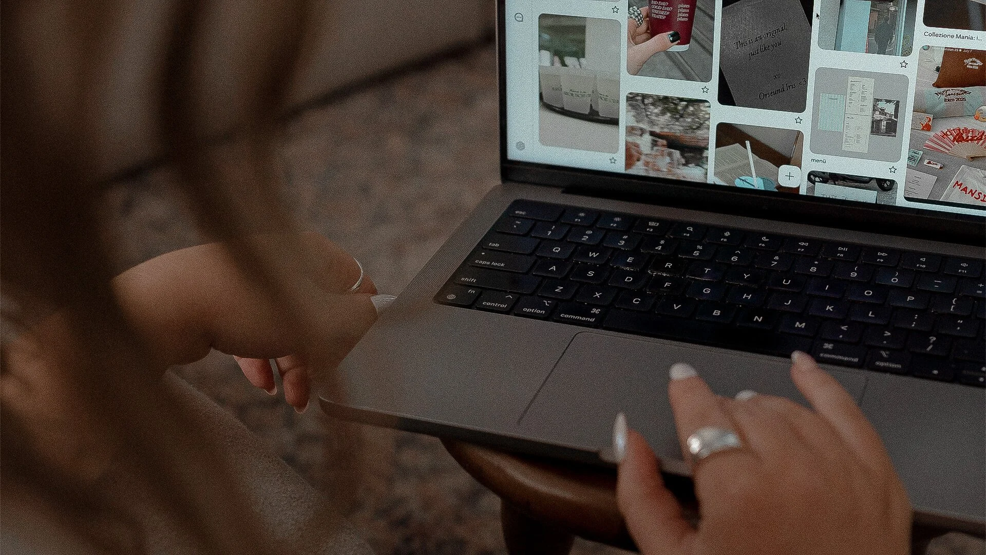 A person with painted nails and rings on their fingers is using a laptop, browsing a digital photo collection or social media app with images of drinks, landscapes, and text.
