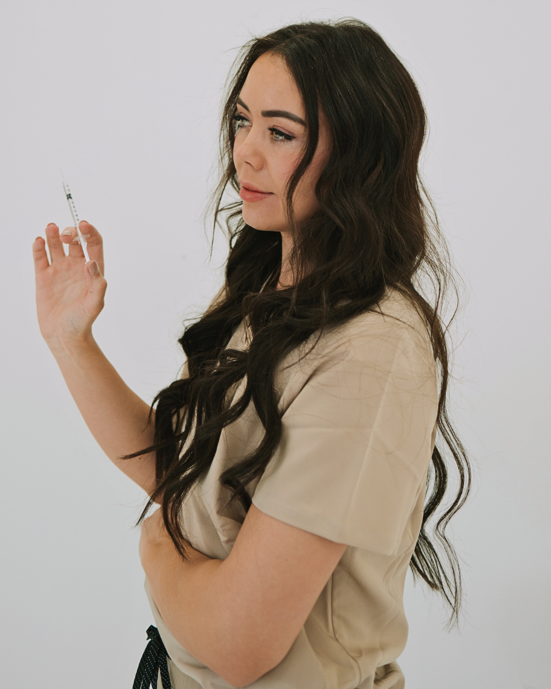 Young woman with long dark hair holding a syringe and looking at it thoughtfully.