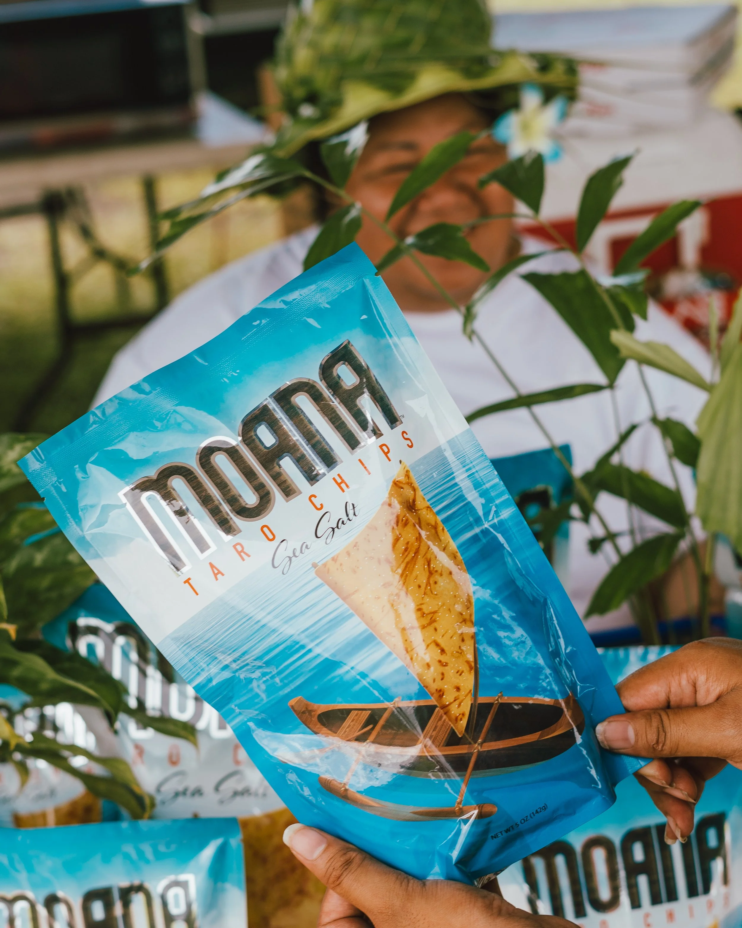 Person holding a bag of moana taro chips and a person with a blurred face in the background.