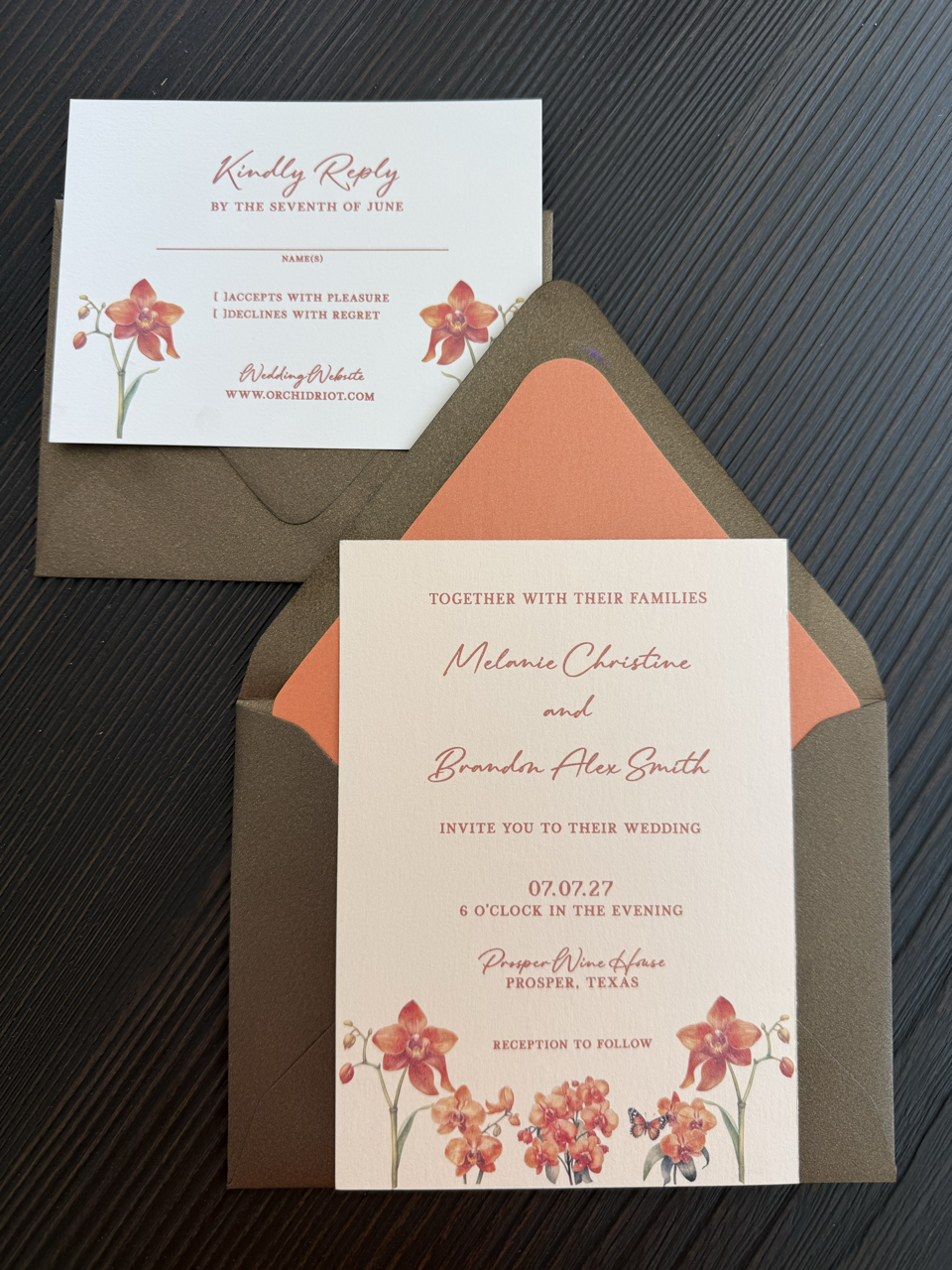 A wedding invitation card with floral designs, placed inside a brown envelope on a black textured surface.