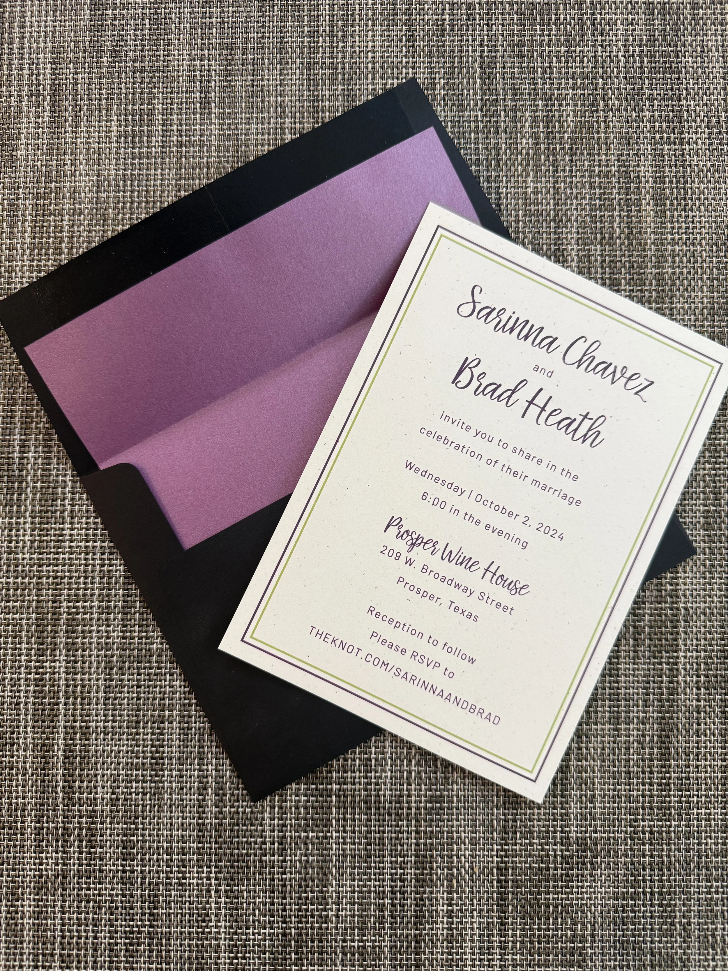Wedding invitation with a white background, purple and black text, and a green border, placed on a textured surface.