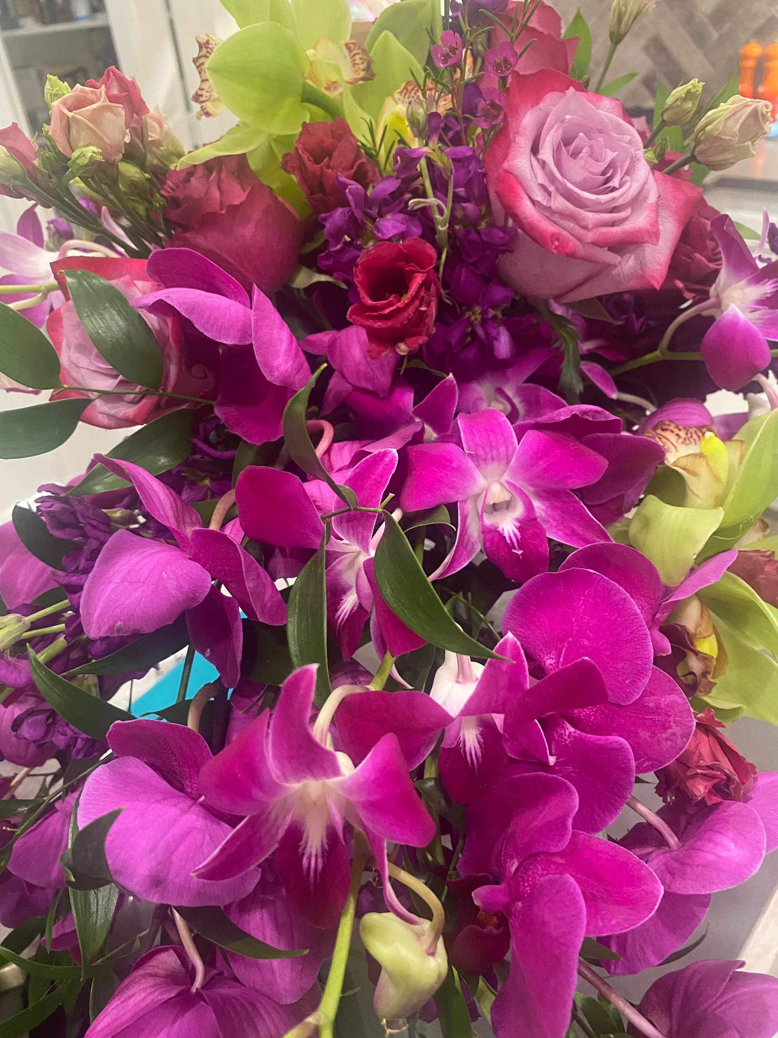 A vibrant bouquet of pink, purple, and green flowers, including roses, orchids, and other assorted blossoms.