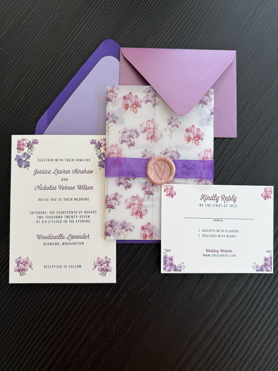 Wedding invitation set with floral theme, featuring purple and pink flowers, a wax seal, and coordinated purple envelopes.