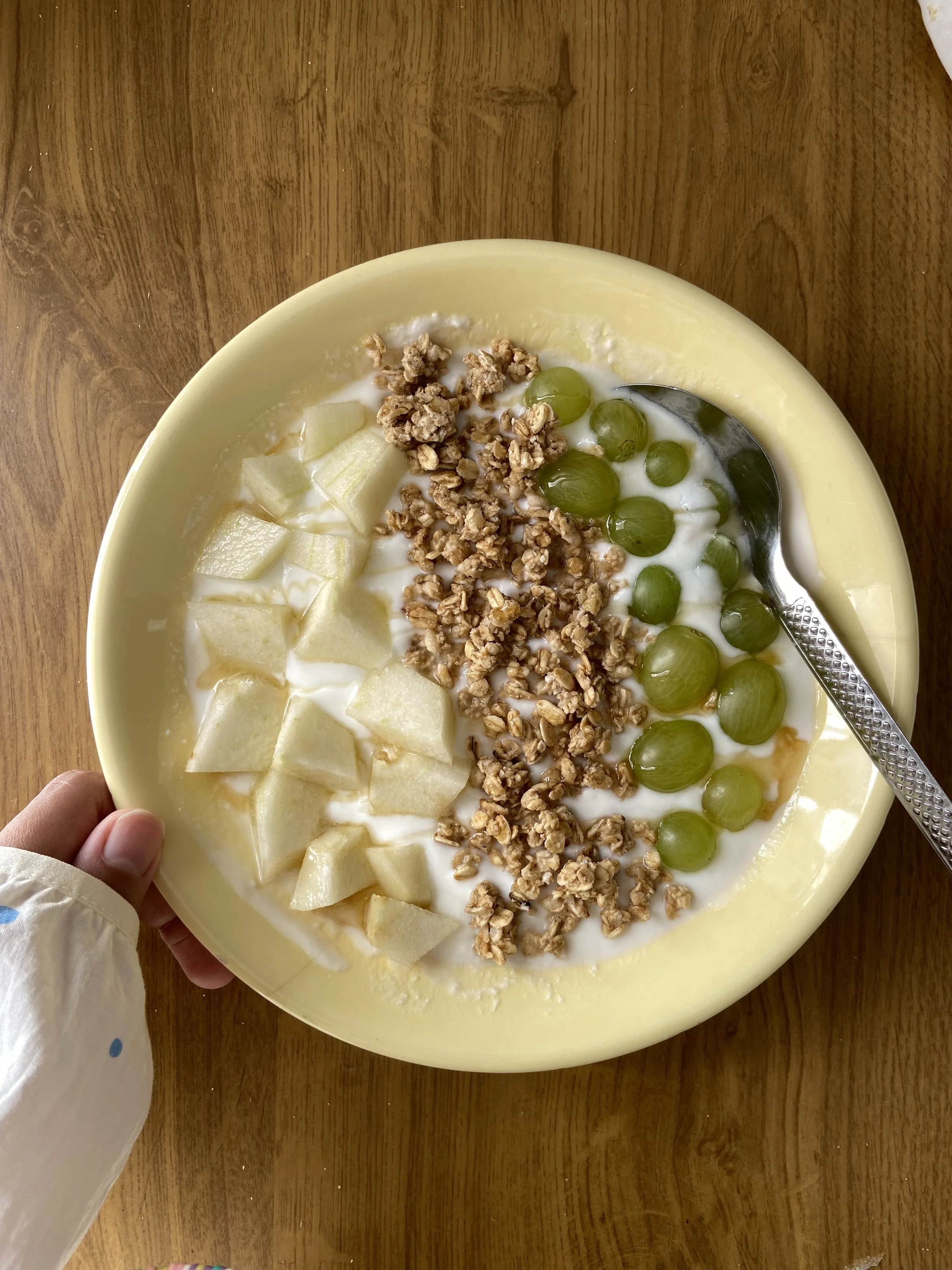 A bowl of yogurt with chopped melon, green grapes, granola, and honey.