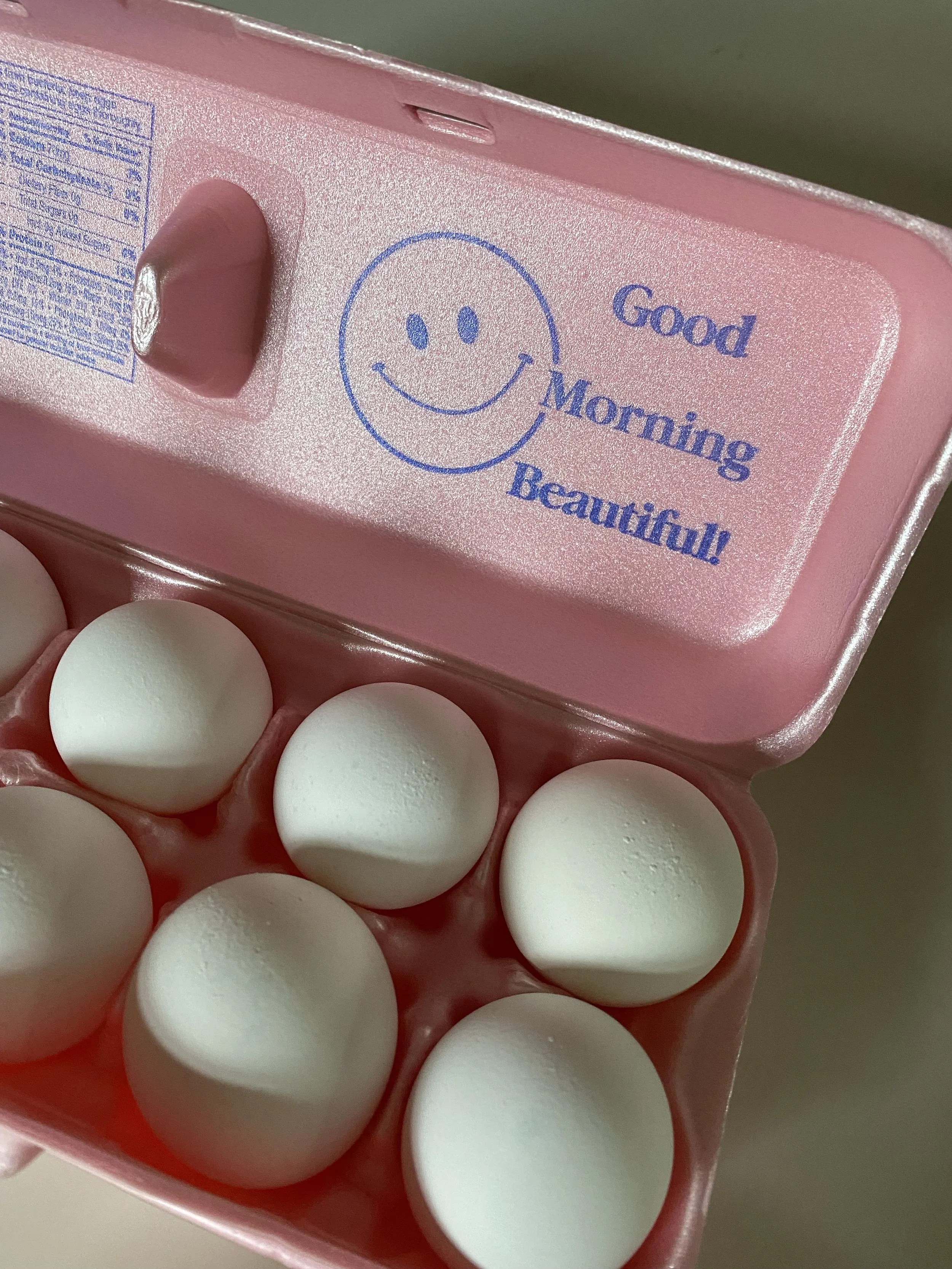 Close-up of a pink egg carton and a smiley face with the words 'Good Morning Beautiful' printed on the inside of the lid.