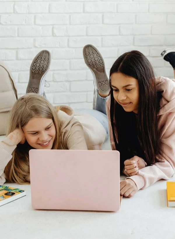 Two teenage girls laying on the ground looking at a laptop representing Sol Sisters K-12 Club
