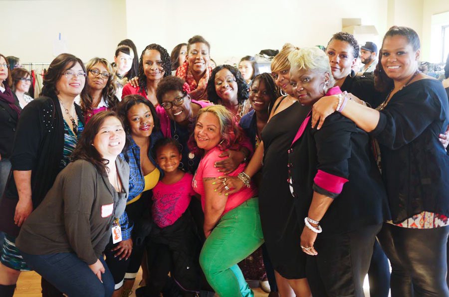 Group of diverse women and children smiling and posing together in a bright indoor space, celebrating together.