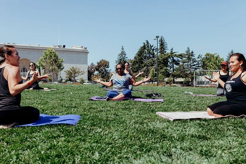 Group of women practicing yoga outdoors on a grassy field.