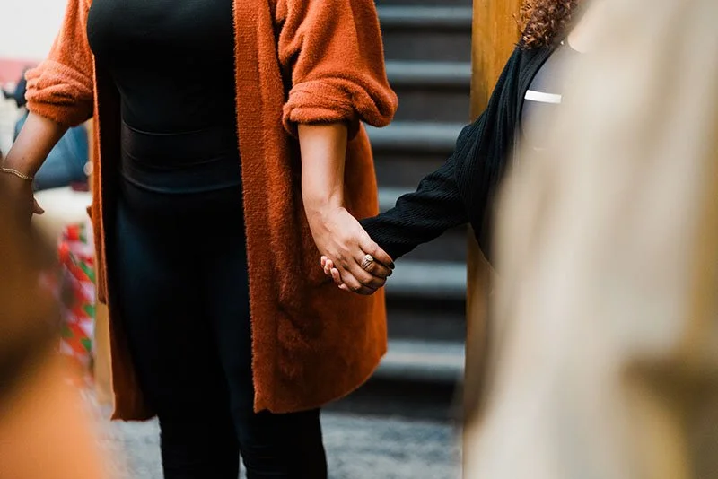 Two women holding hands, standing close together in an indoor setting.