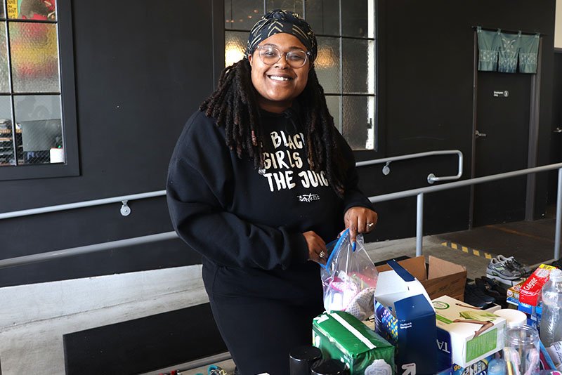 Smiling woman with glasses and a headscarf shopping at a table with various groceries
