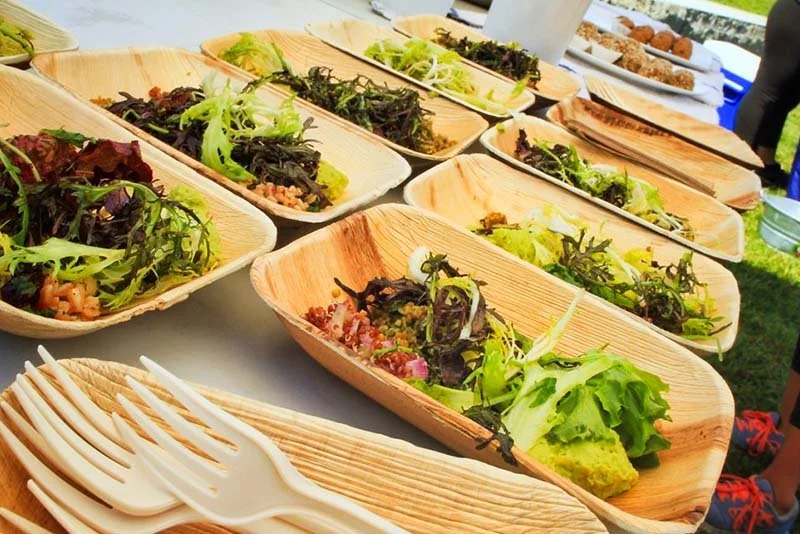 Multiple wooden bowls with various salads and a pile of disposable forks.