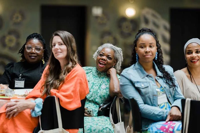 Group of women sitting at a conference table, smiling and laughing