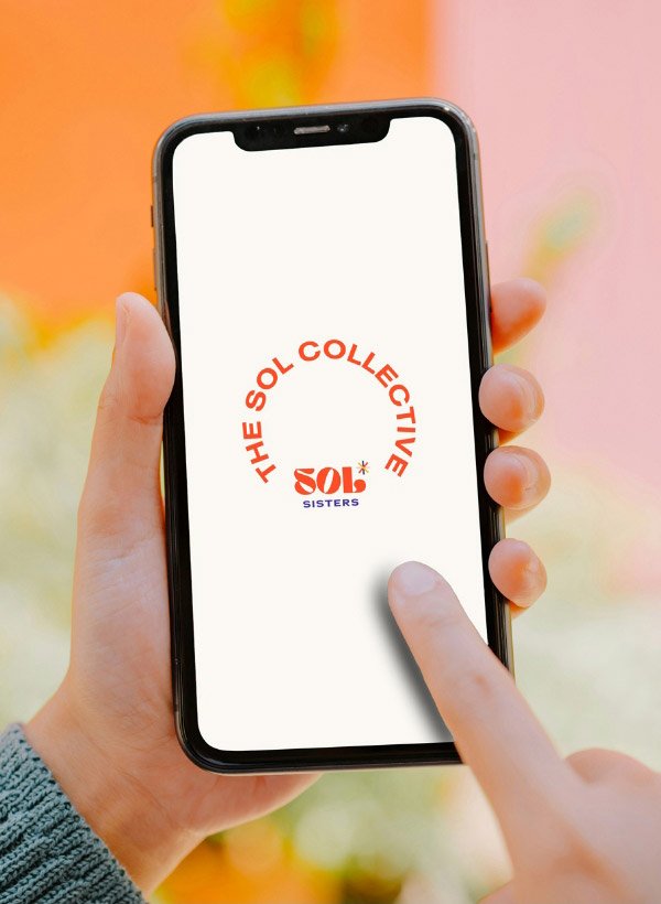 A woman's hands holding an iphone that shows the Sol Collective Sol Sisters logo
