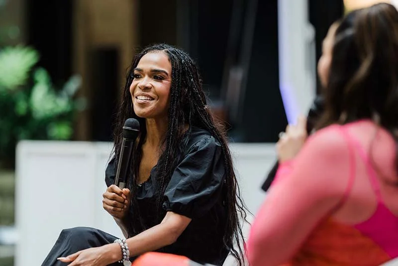A woman with long dark hair smiling and holding a microphone during a discussion or interview.