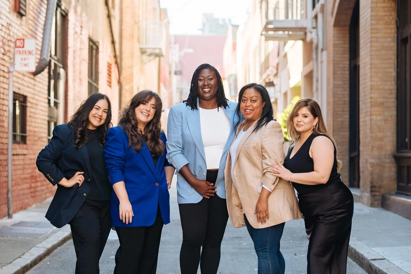 Group of five women standing in a city alley, smiling at the camera.