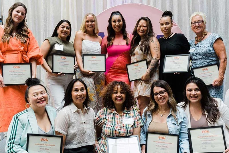 Group of diverse women holding certificates, celebrating at an indoor event.