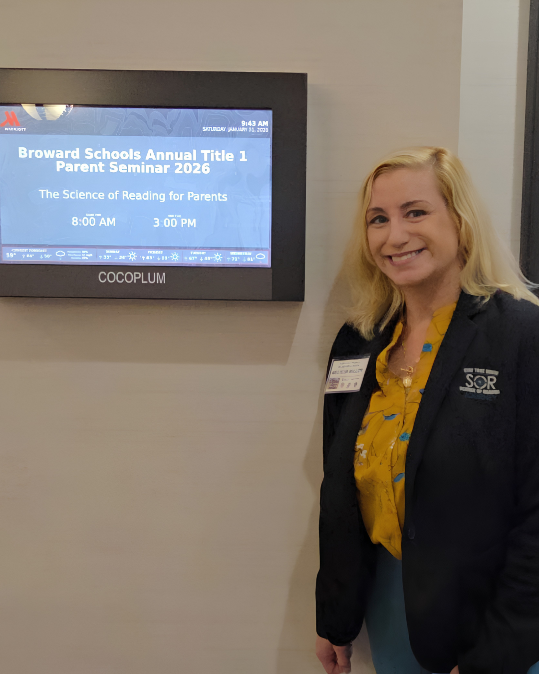 Woman smiling at conference with digital display screen showing 'Broward Schools Annual Title 1 Parent Seminar 2026' and schedule from 8:00 AM to 3:00 PM.