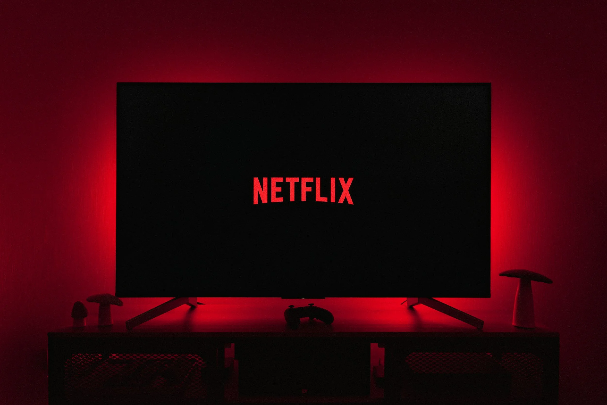 A black television screen with red 'Netflix' logo on it, placed on a stand in a dark room with red lighting.