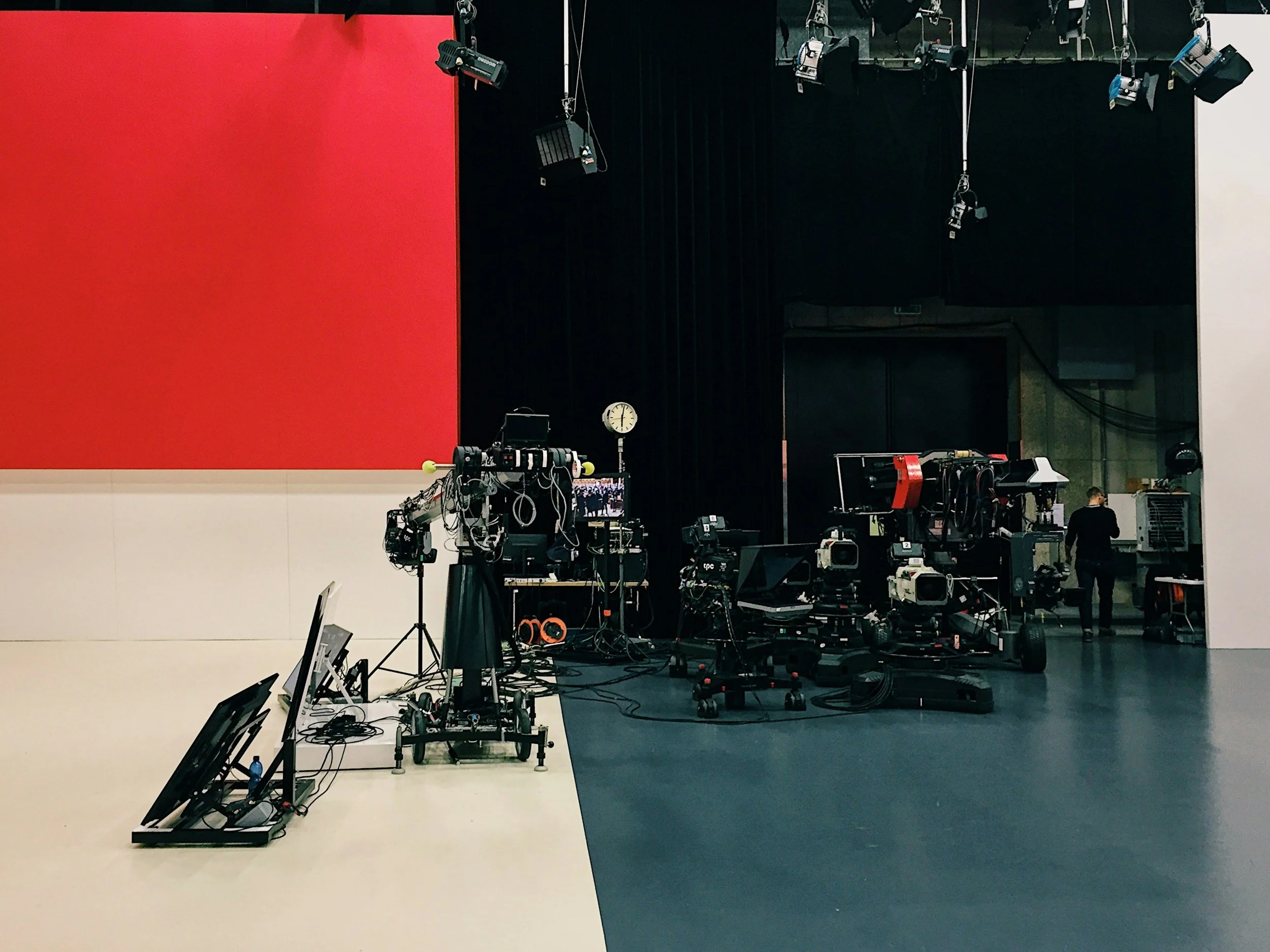 Empty stage with red and black background, various engineering and photography equipment set up in the foreground, including cameras, tripods, lights, and cables.