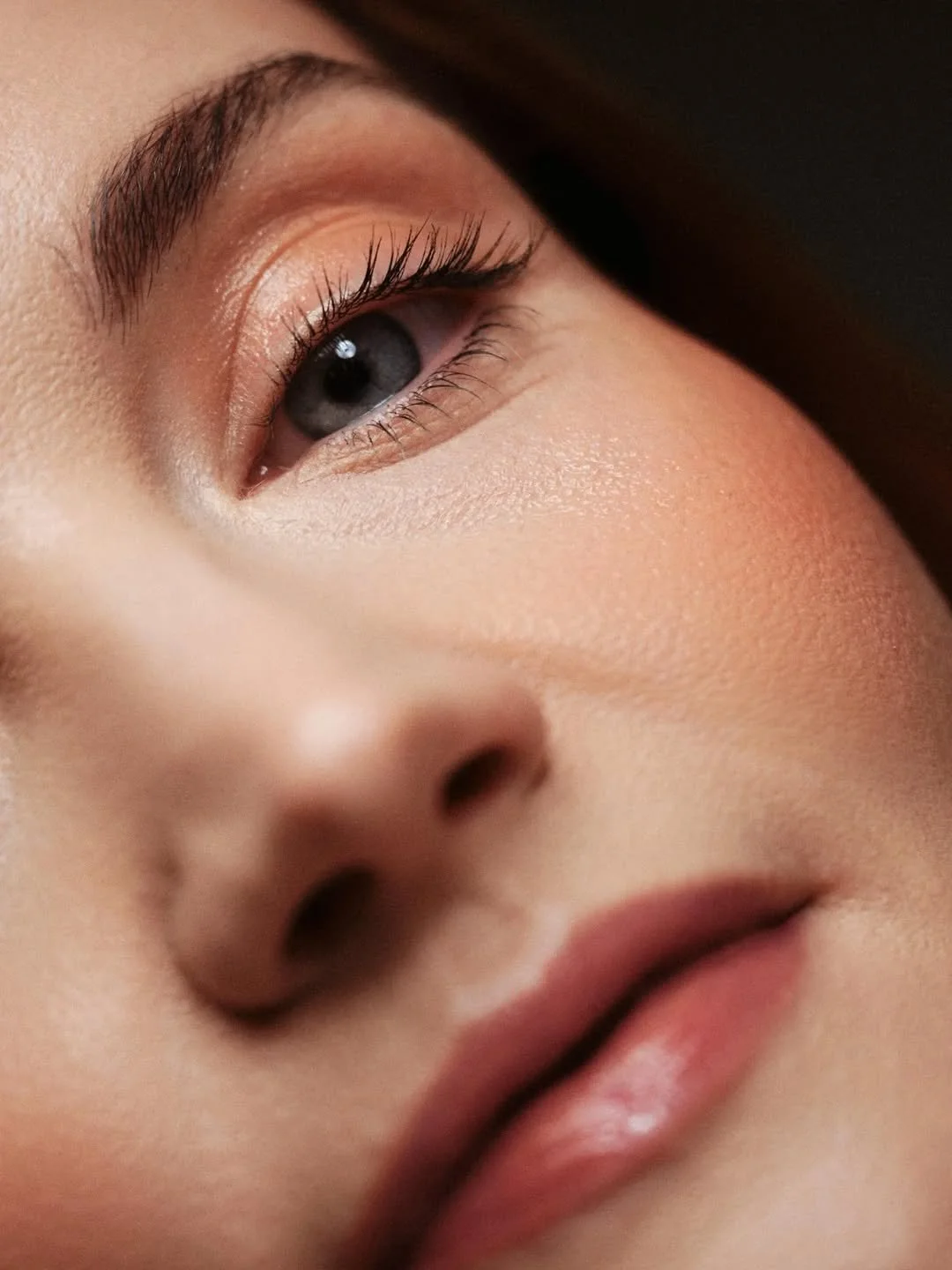 Close-up of a woman's face focusing on her eye, nose, and lips, with makeup and natural skin texture.