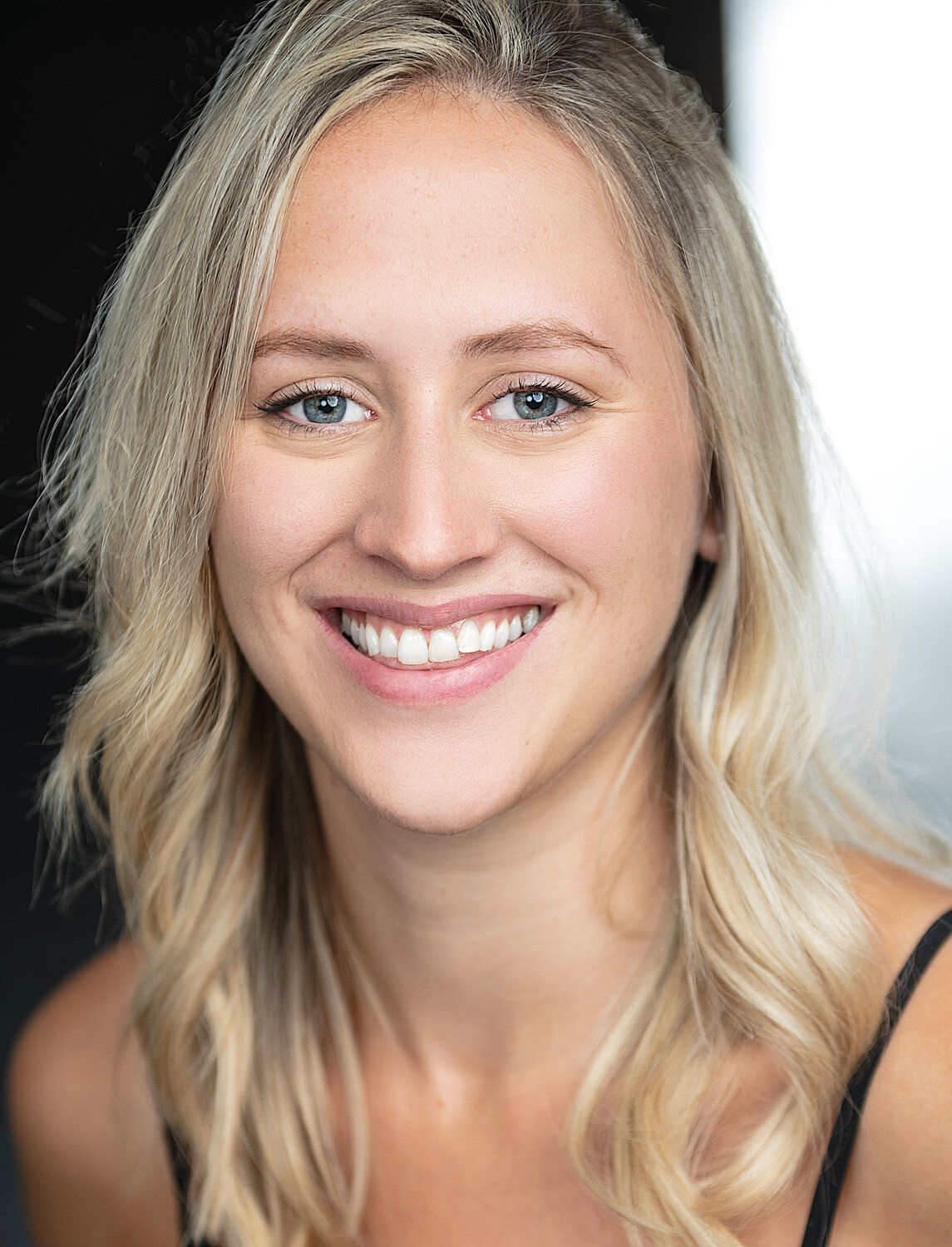 Close-up portrait of a smiling young woman with blonde hair and blue eyes.