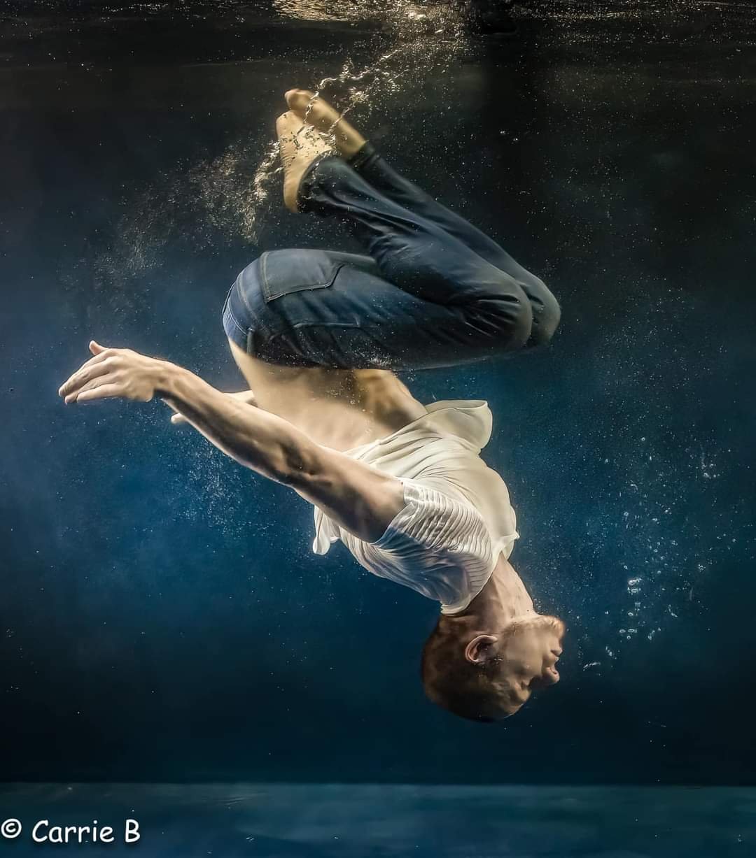 A man falling underwater with a white shirt and dark pants, captured mid-descent with bubbles around him.